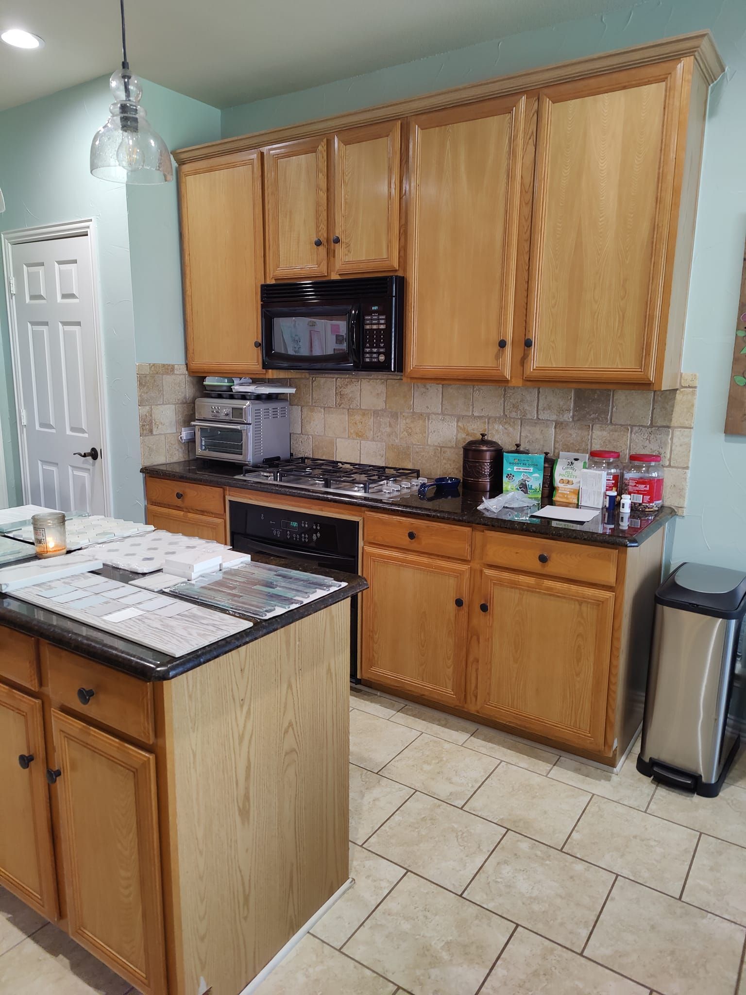 Kitchen with wooden cabinets, a stovetop, and an island. Beige tile backsplash and light blue walls.