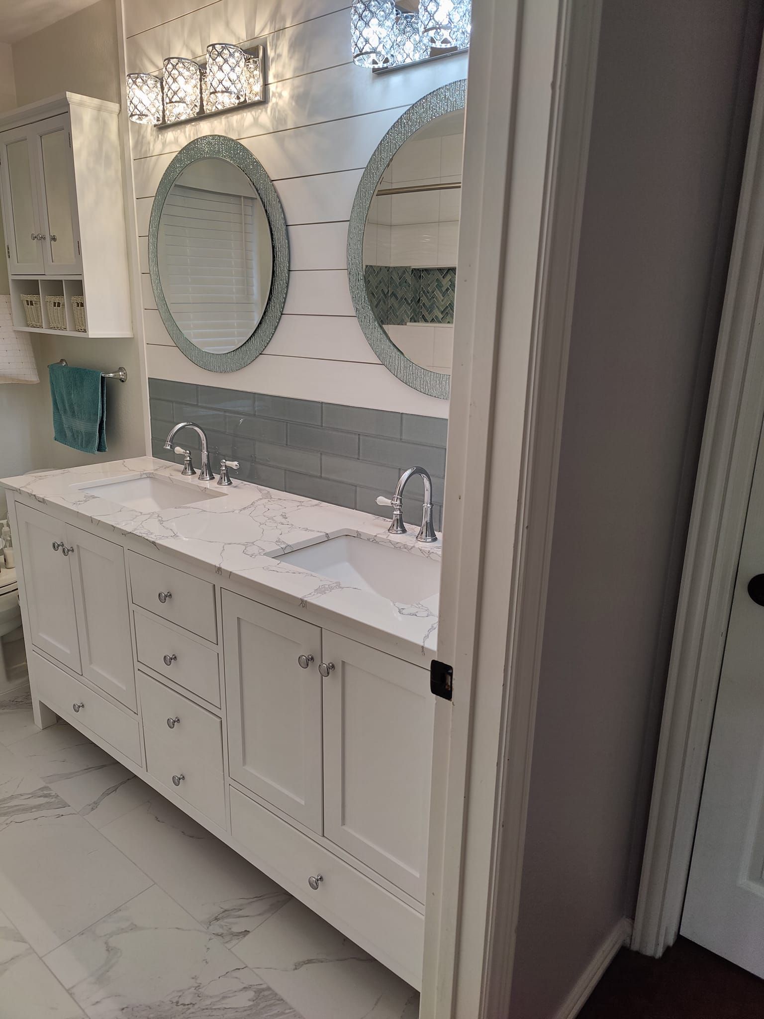 White bathroom with a double vanity, round mirrors, and silver fixtures.