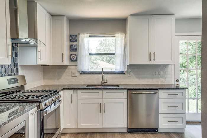 White kitchen with stainless steel appliances, white cabinets, and dark countertops.