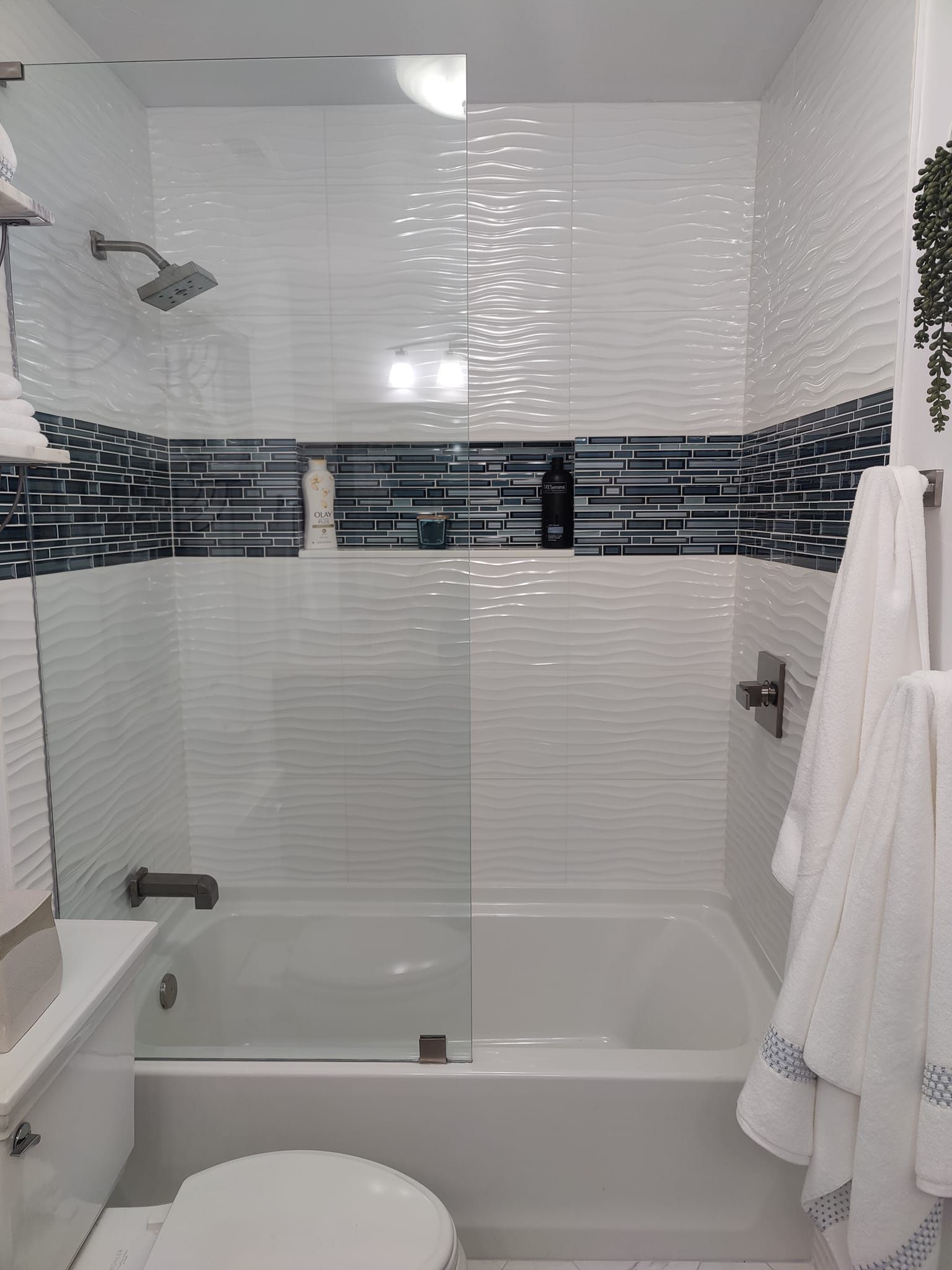 Bathroom with white bathtub, glass shower door, and decorative white and blue tile.