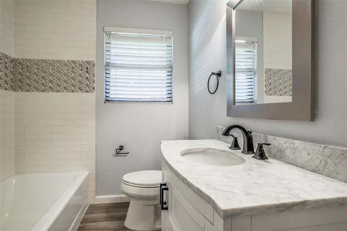 Bathroom with a white vanity, marble countertop, and a white bathtub. Light gray walls and tile accents.
