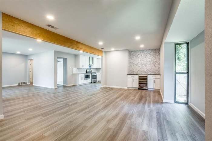 Bright open living room with wood floors, white walls, kitchen pass-through, and large windows.
