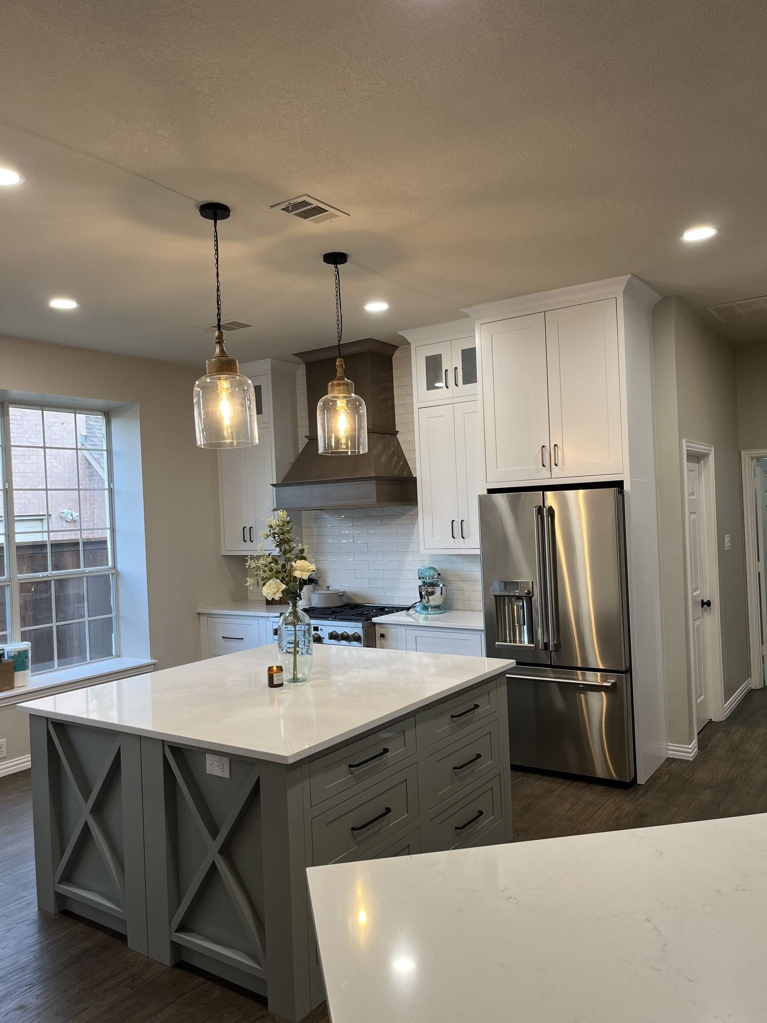 Kitchen with gray island, white cabinets, stainless steel appliances, and pendant lights.