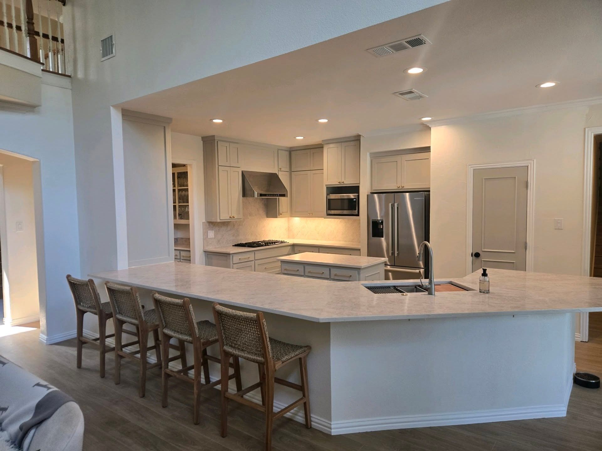 A modern kitchen with light gray cabinets, white countertops, and bar seating.