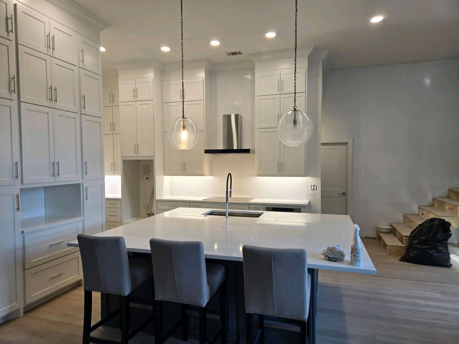 White kitchen with island, cabinets, and pendant lights. Barstools at island.