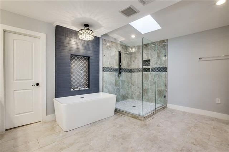 Modern bathroom with a white tub, walk-in shower, and skylight. Blue accent wall, gray tile.