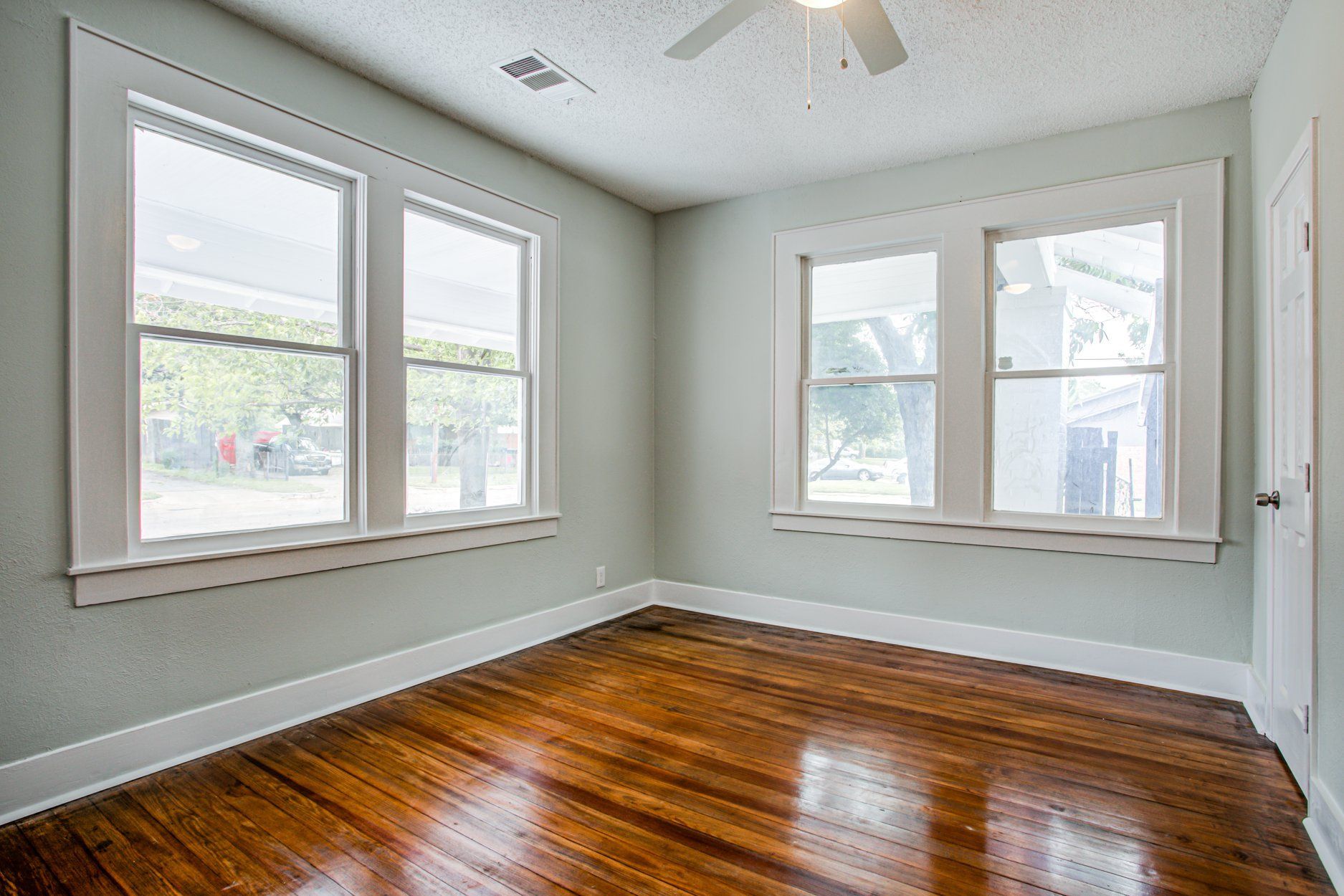 Empty room with hardwood floor, three windows, and white trim.