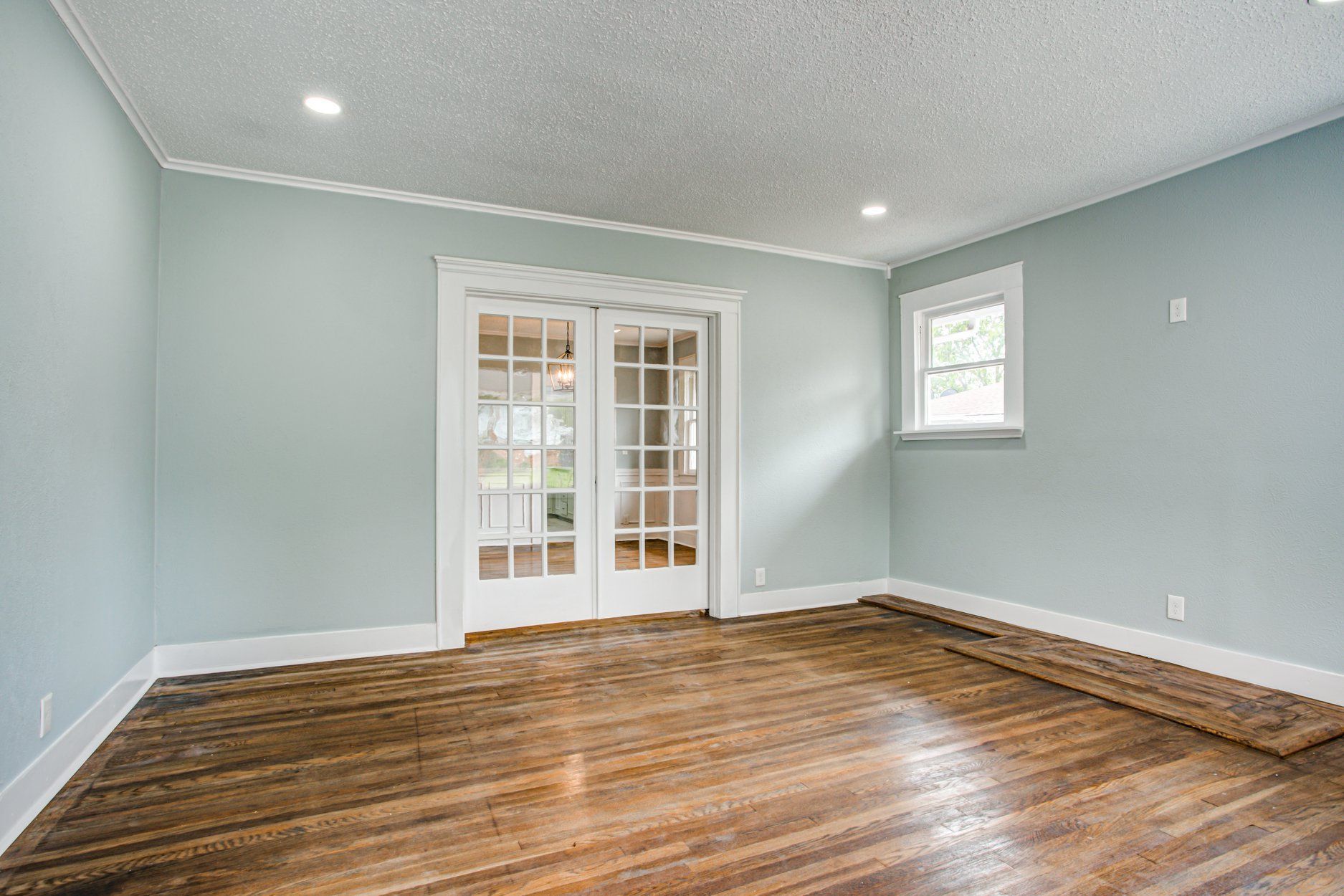 Empty room with wooden floors, light blue walls, and white French doors.