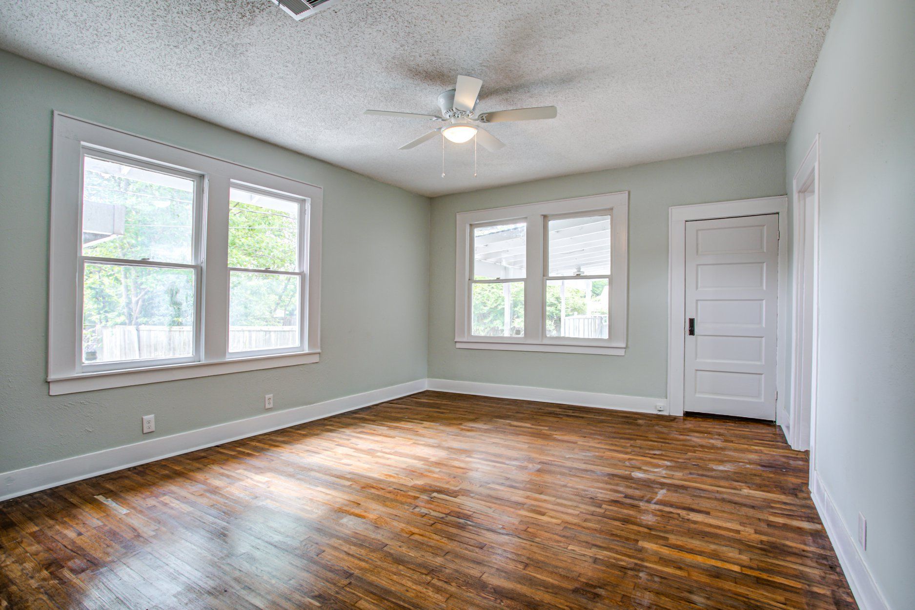 Empty room with hardwood floors, light blue walls, white trim, and a ceiling fan.
