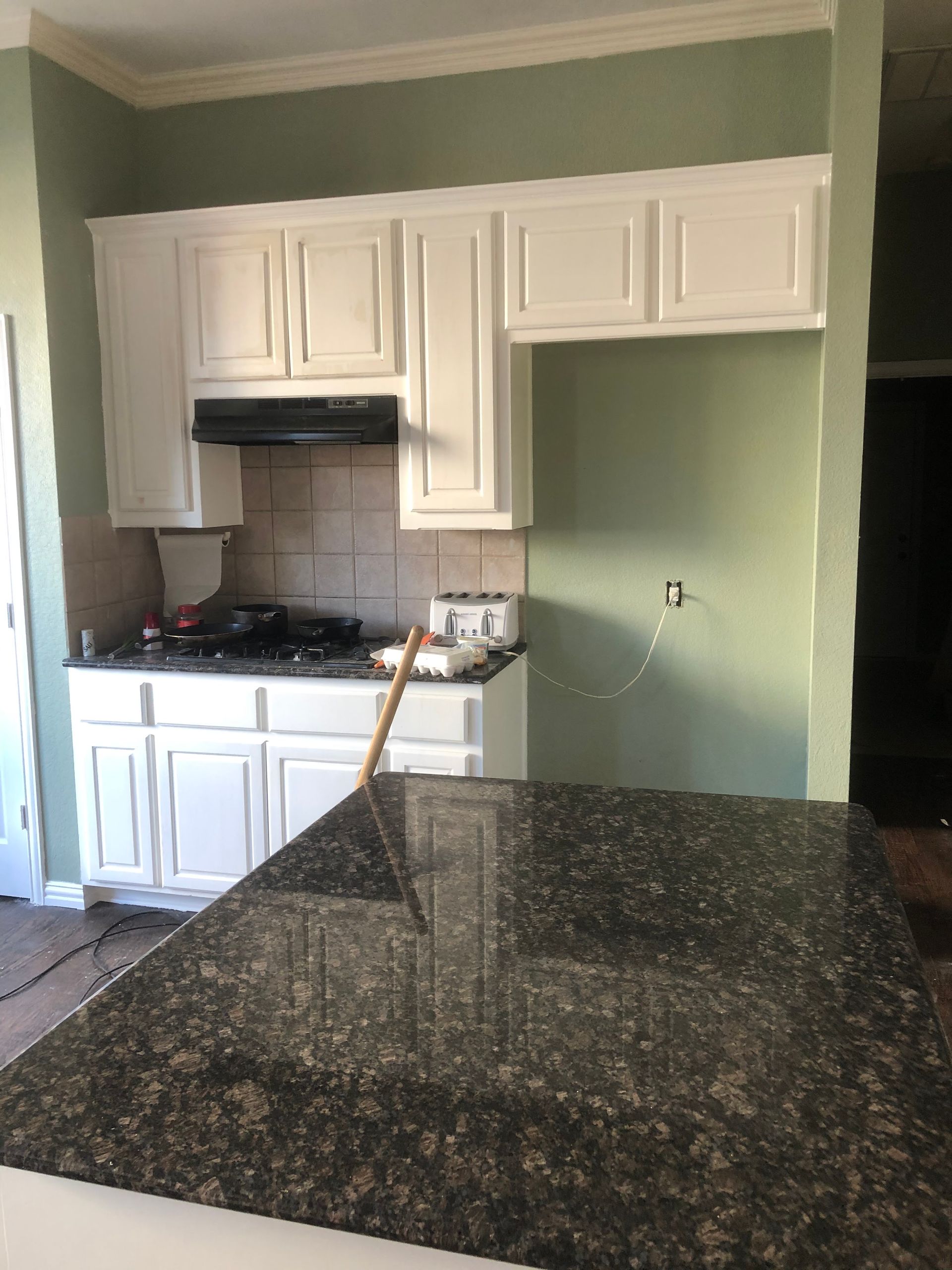 White kitchen cabinets with black granite countertop, green walls.