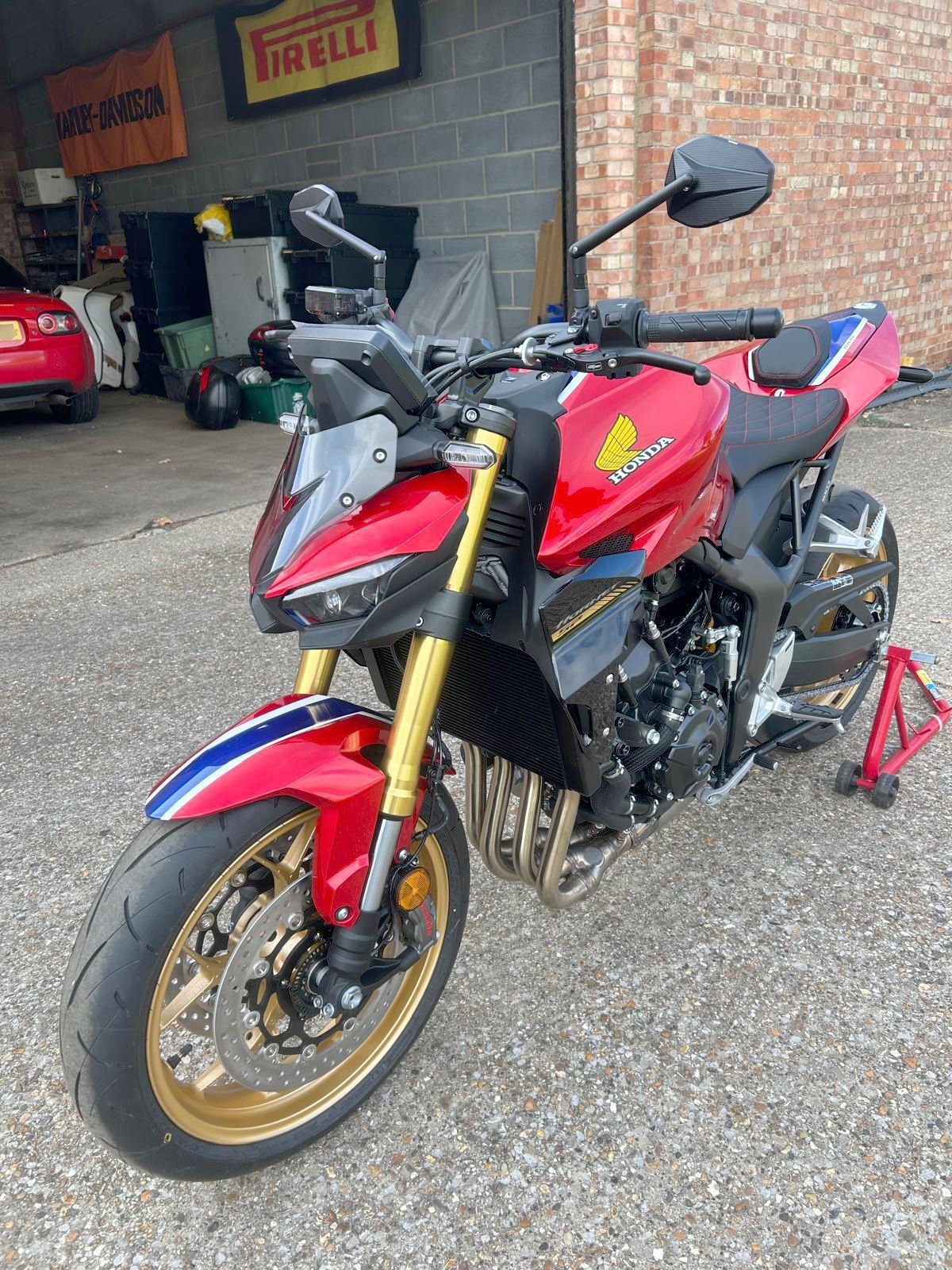 Red and gold Honda motorcycle with blue and white stripes parked in front of a garage.