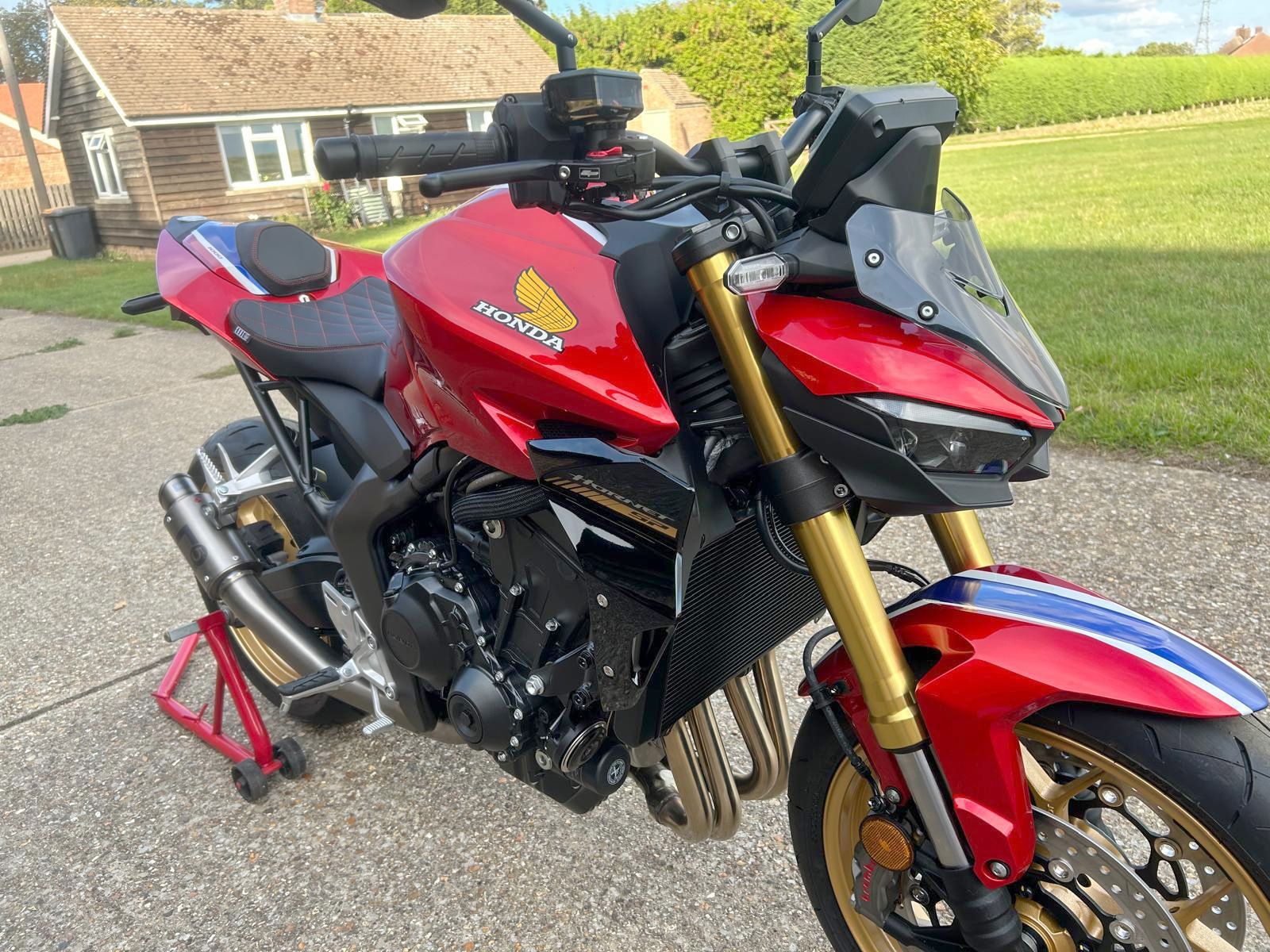 Red and black Honda motorcycle parked on a driveway, gold accents, red stand, bright setting.