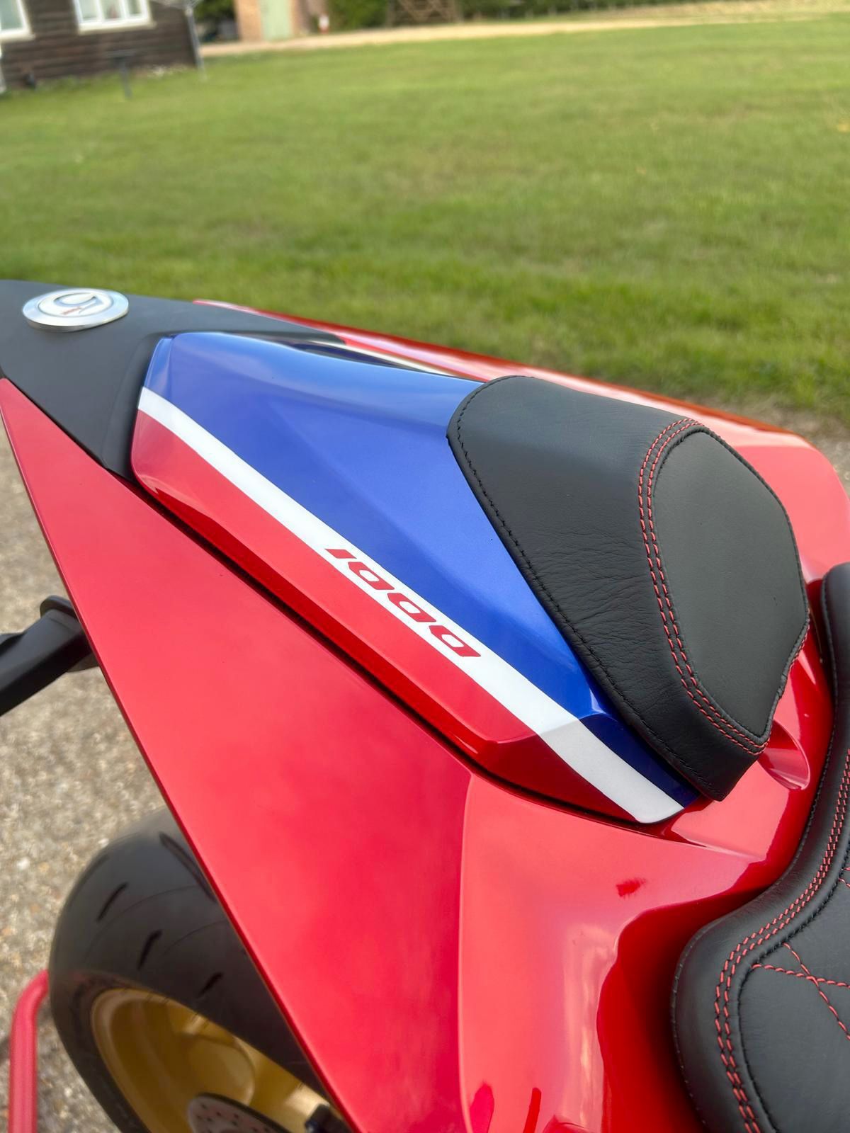 Red, white, and blue motorcycle seat with black padding, “1000” logo, and red stitching on a red motorcycle.