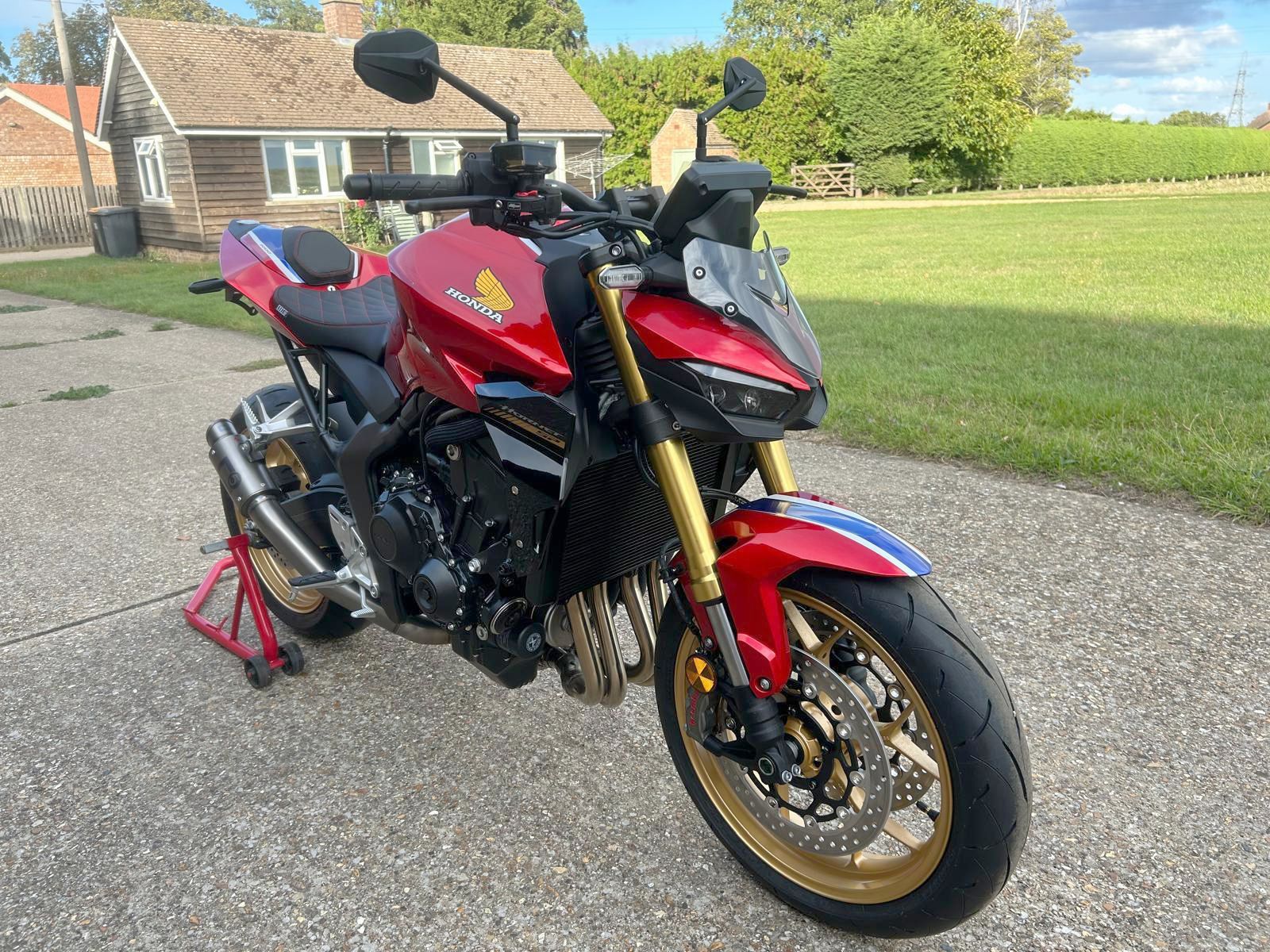 Red and black Honda motorcycle parked outside a rural house on a sunny day.