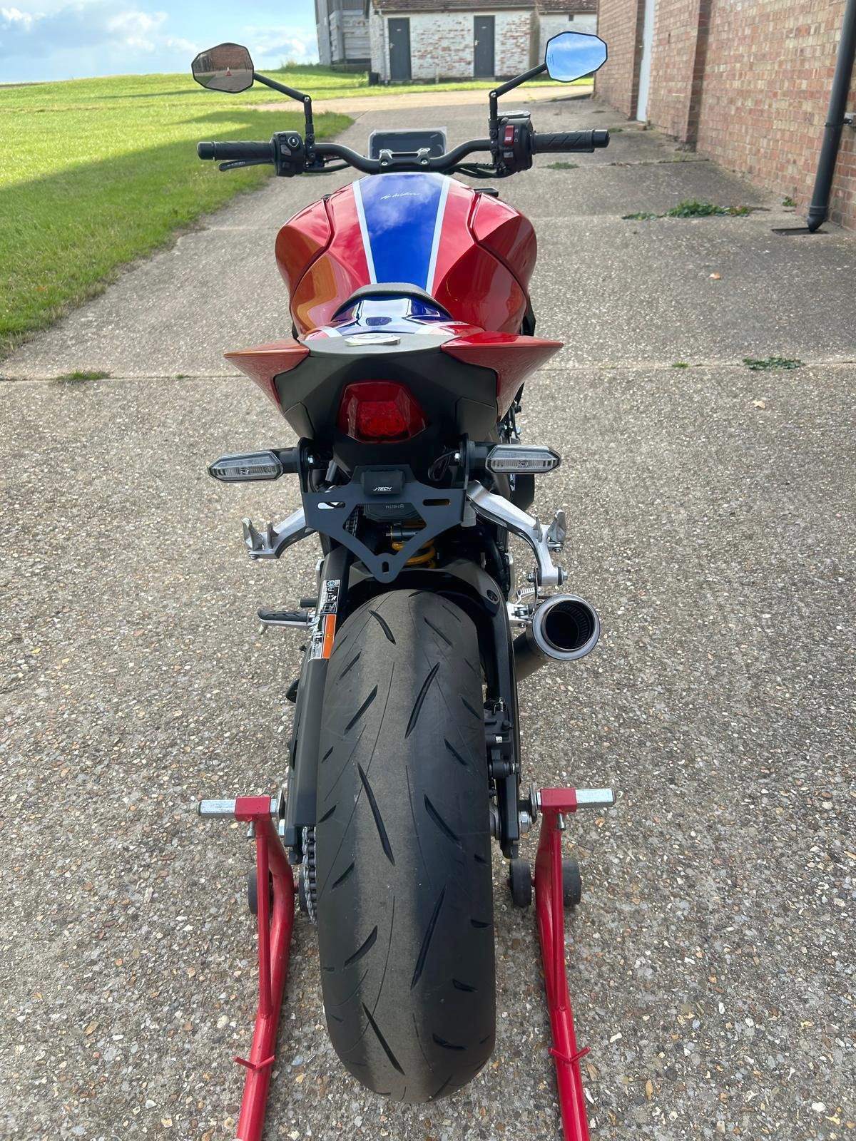 Rear view of a red, white, and blue motorcycle on a stand. Dark tire, black exhaust.