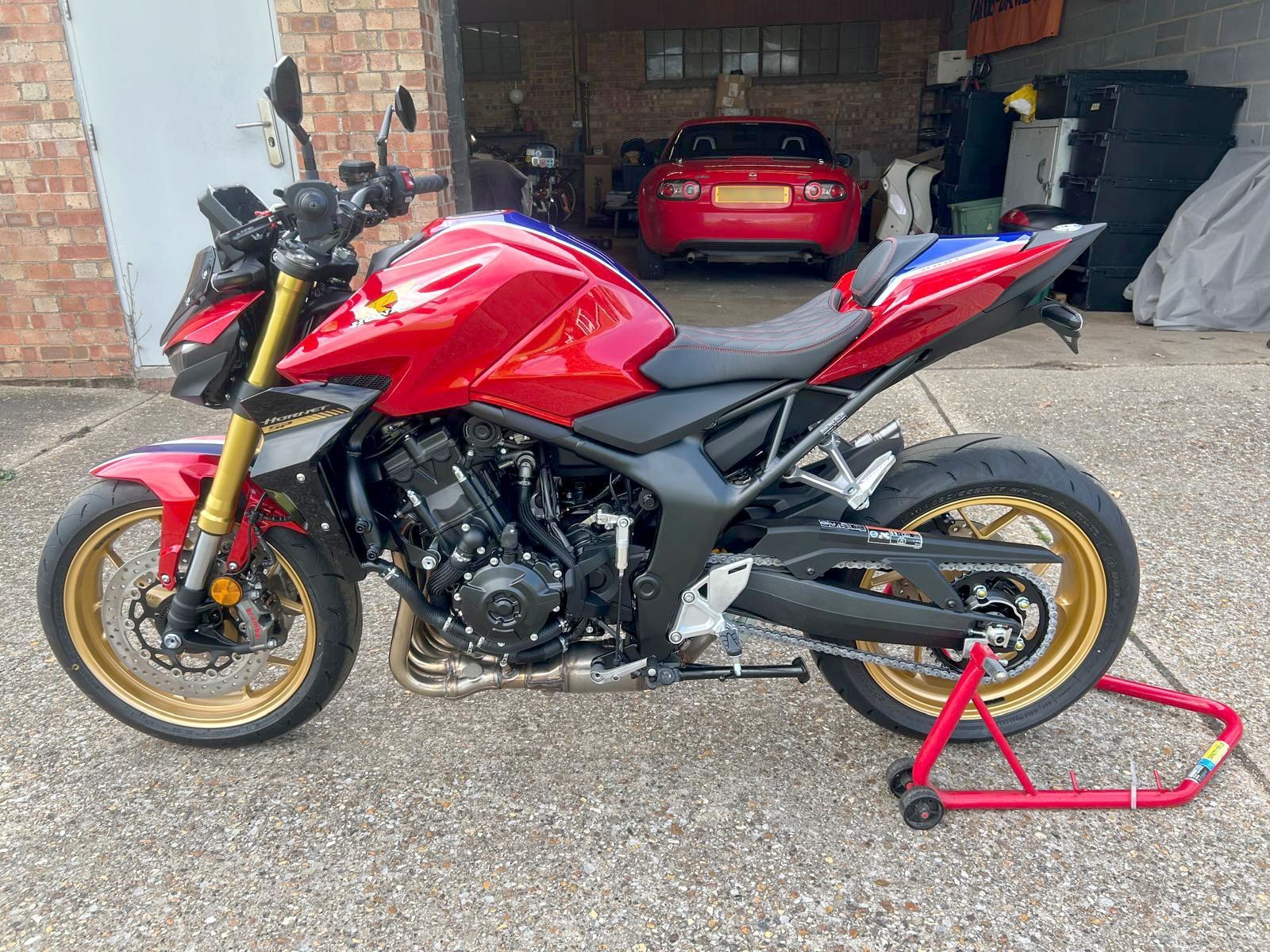 Red and black Honda motorcycle with gold accents, parked in front of a garage.
