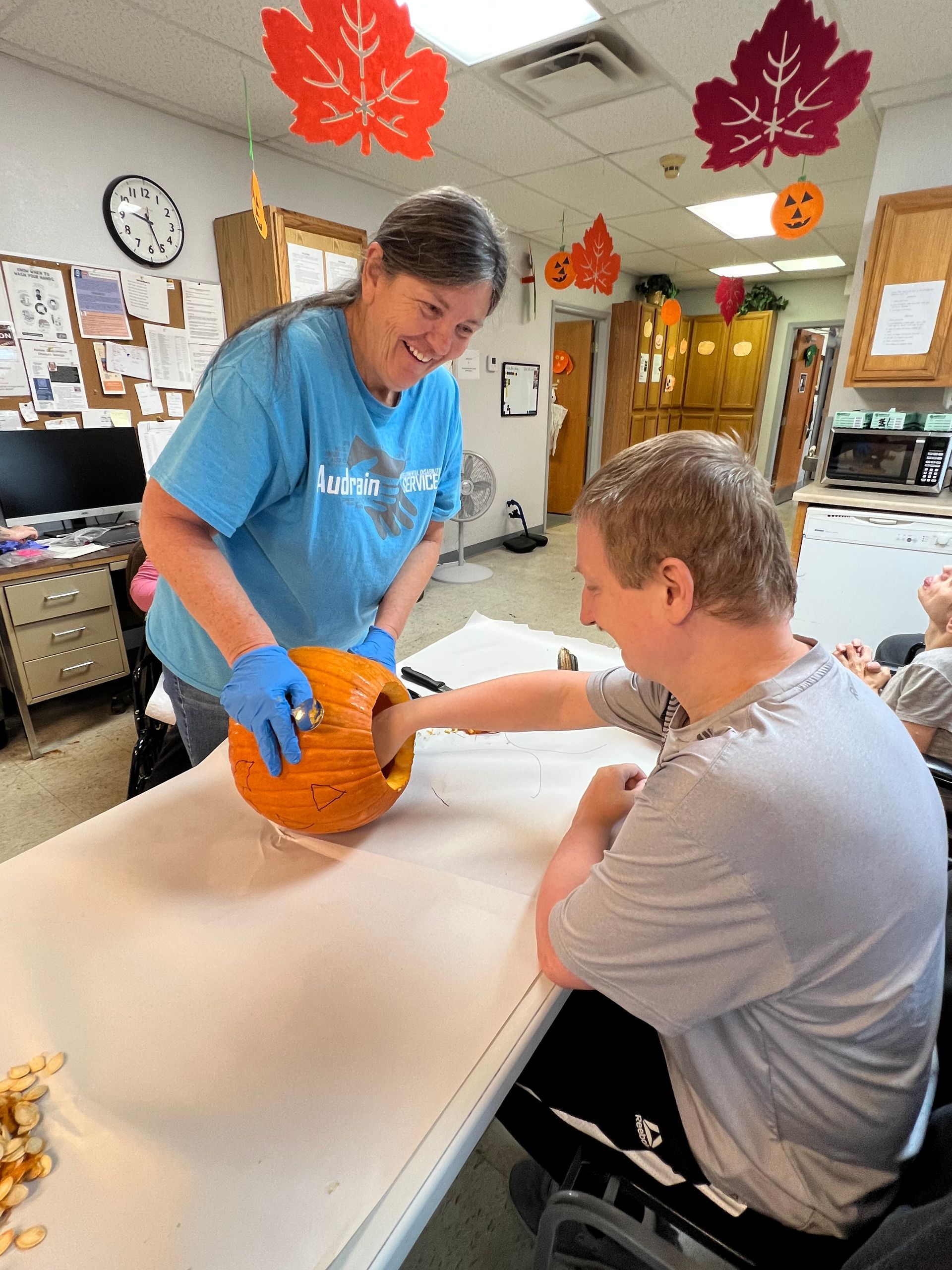 a woman in a blue shirt that says audrain on it is carving a pumpkin