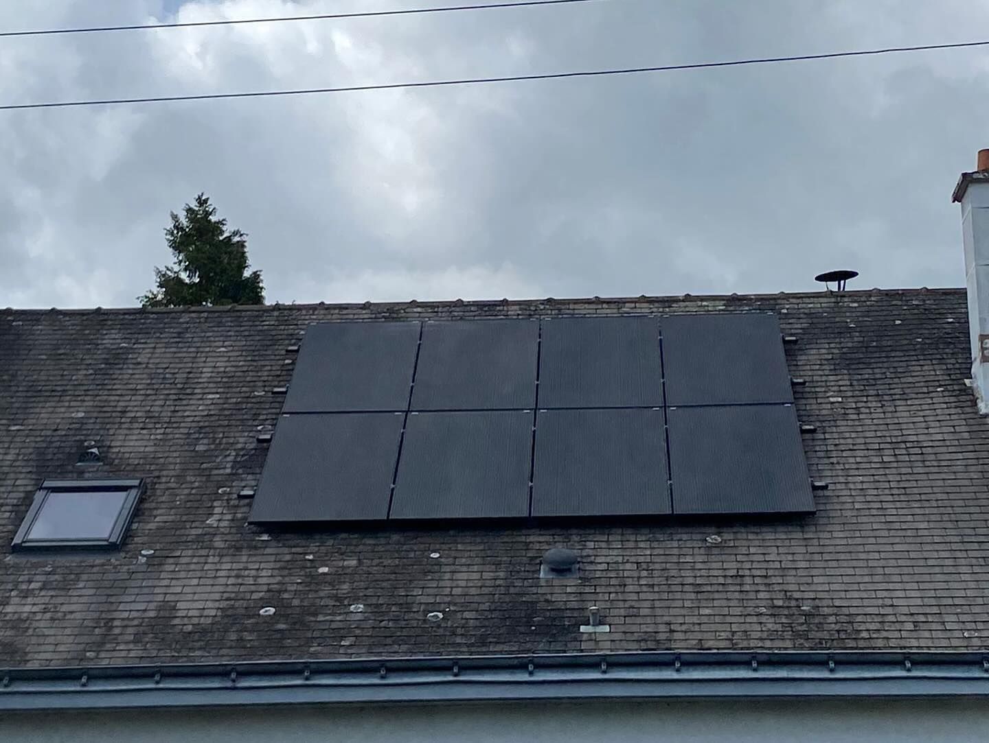 Panneaux solaires installés sur le toit d'une maison aux bardeaux gris sous un ciel nuageux