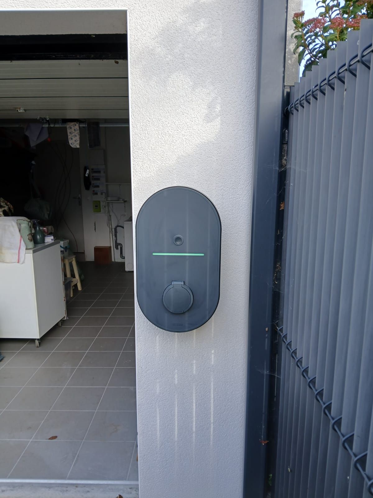 Dispositif mural sombre avec une ligne lumineuse sur un mur extérieur blanc, à côté d'un garage ouvert.