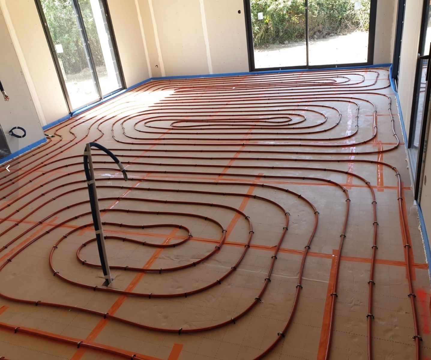 Des tuyaux de chauffage au sol orange sont disposés en boucles sur le sol d'une pièce en construction.