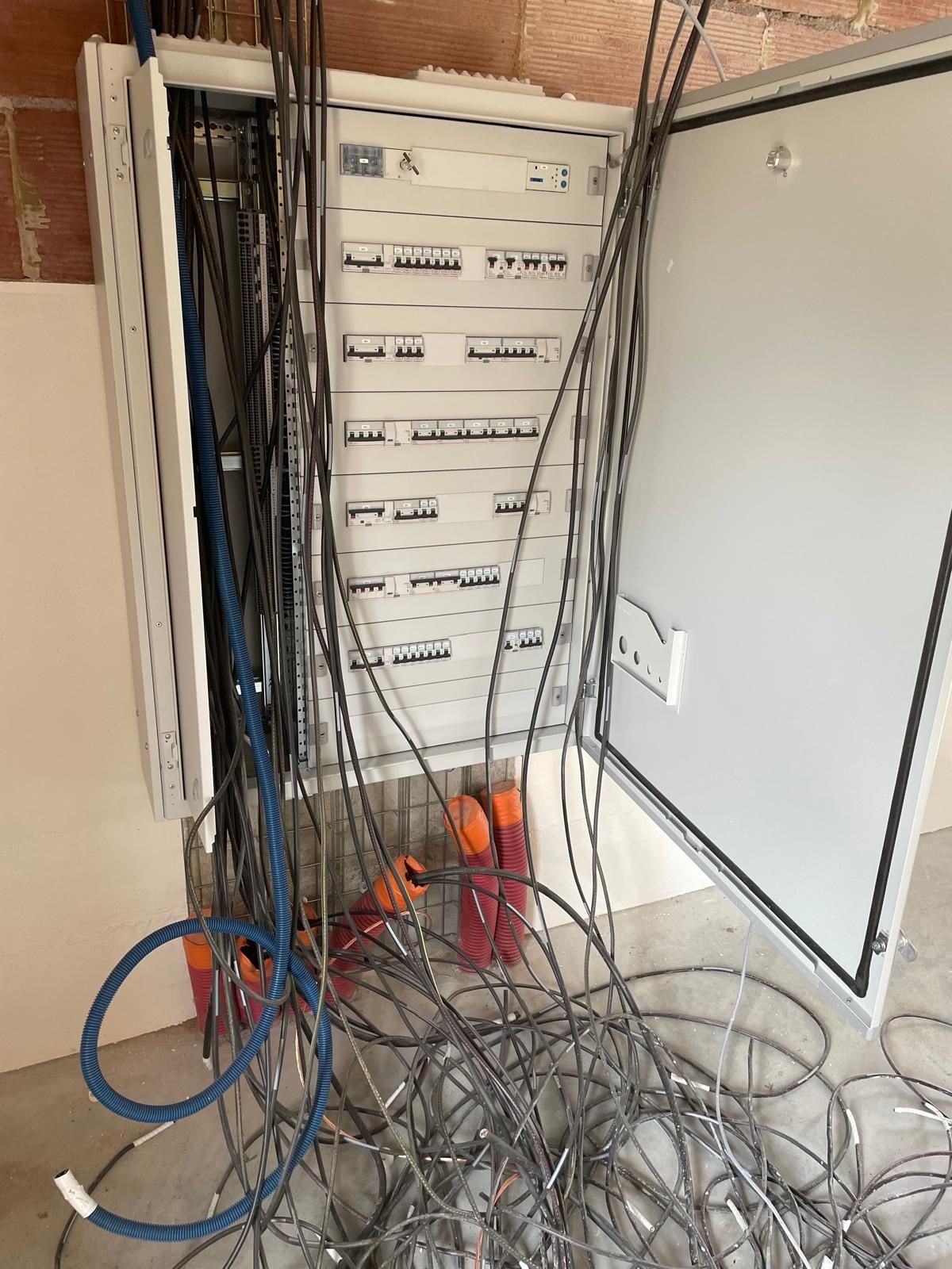 Tableau électrique ouvert avec câbles emmêlés et fils dénudés dans une buanderie