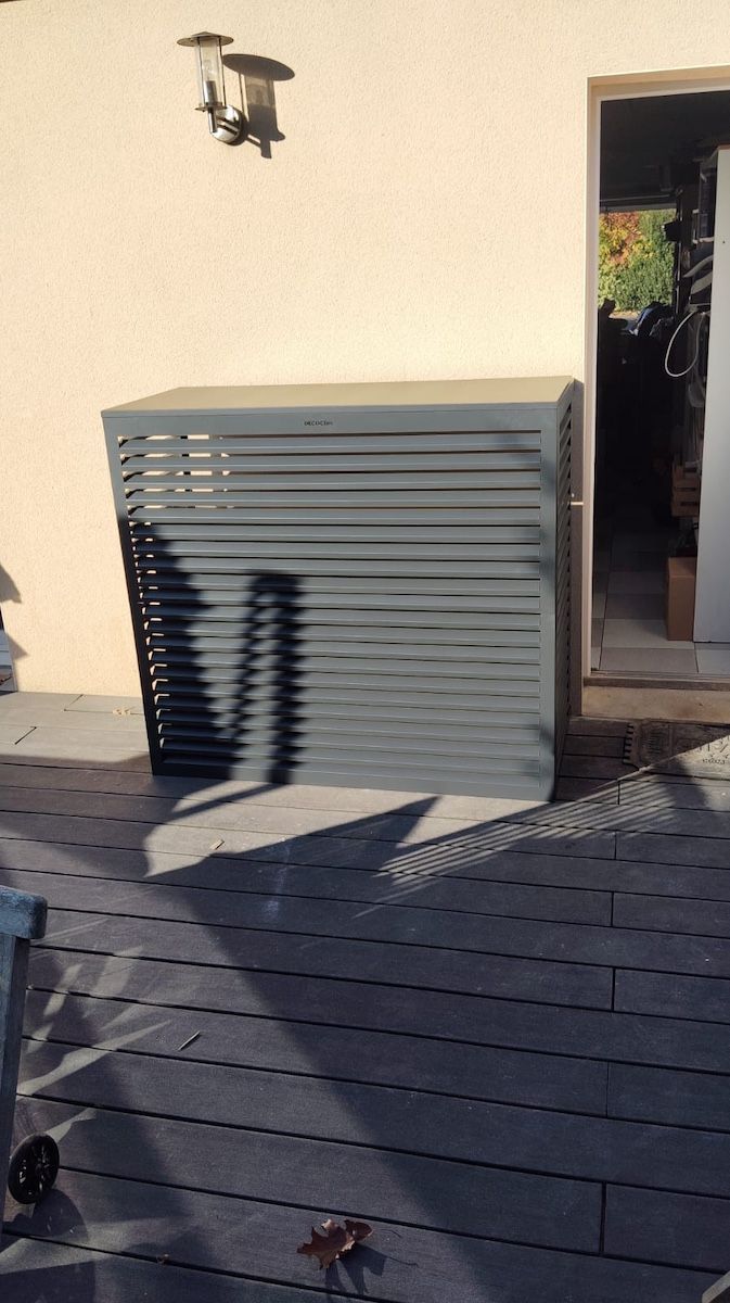 Terrasse extérieure avec un meuble de rangement gris à côté d'une porte ouverte, projetant des ombres sur la terrasse.