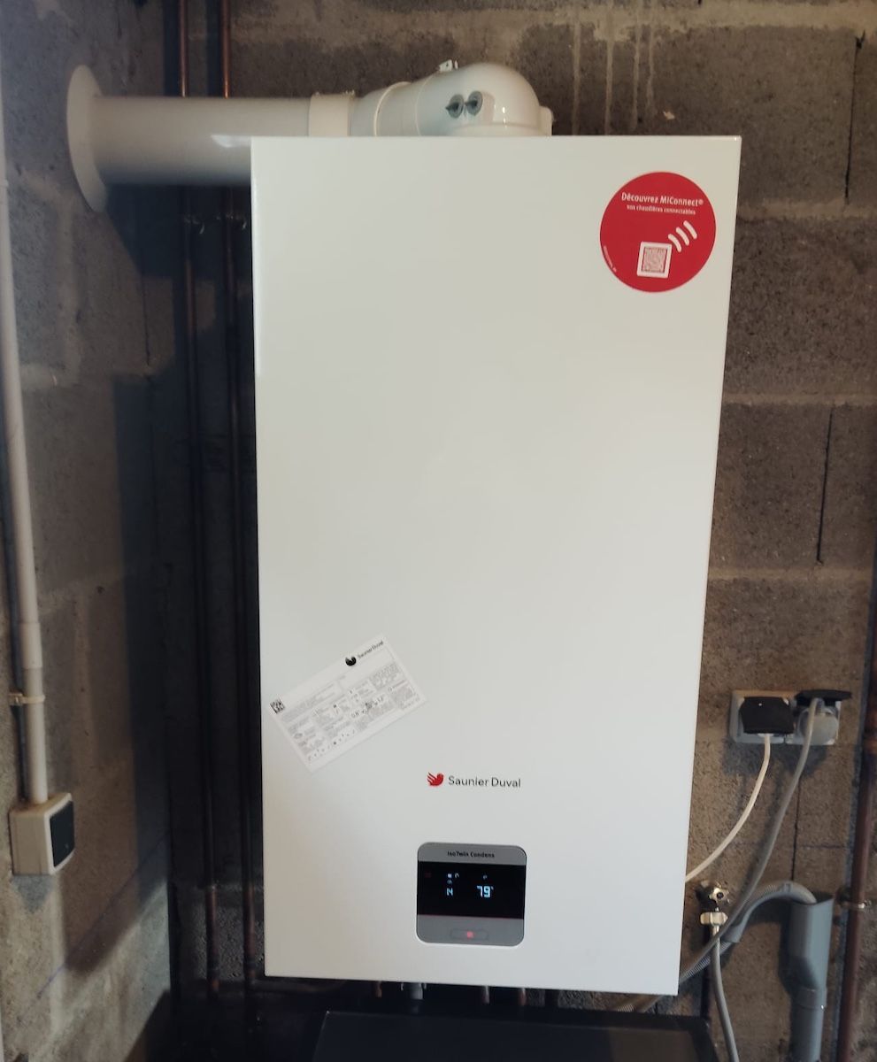 Chaudière murale blanche dans une buanderie, avec tuyaux et étiquette autocollante rouge.