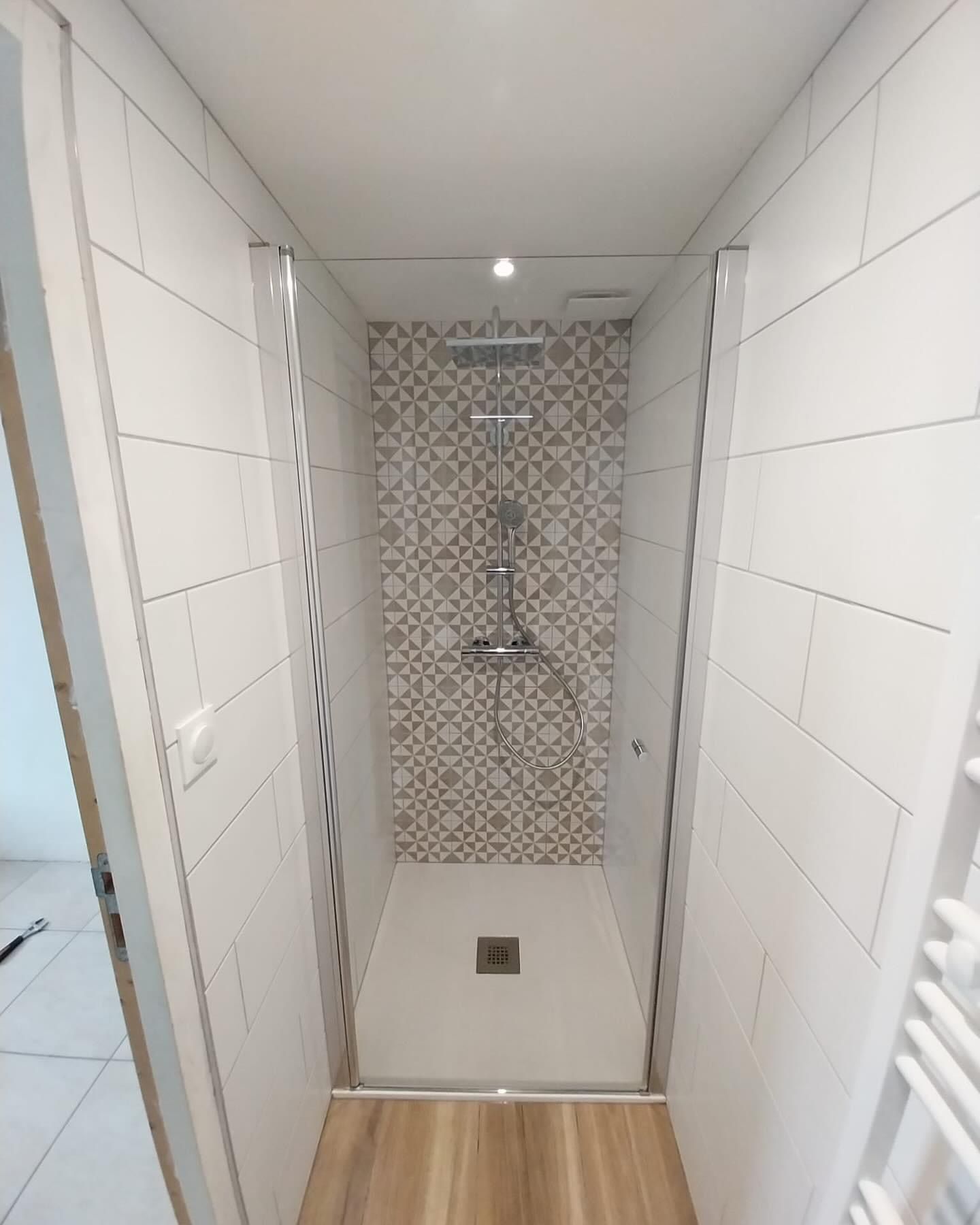 Cabine de douche étroite carrelée avec murs blancs, carrelage mural à motifs et éclairage au plafond.
