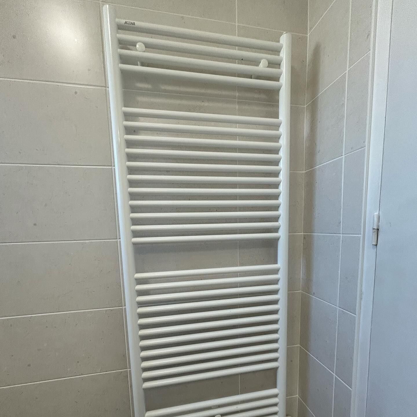 Radiateur sèche-serviettes mural blanc dans une salle de bains carrelée.