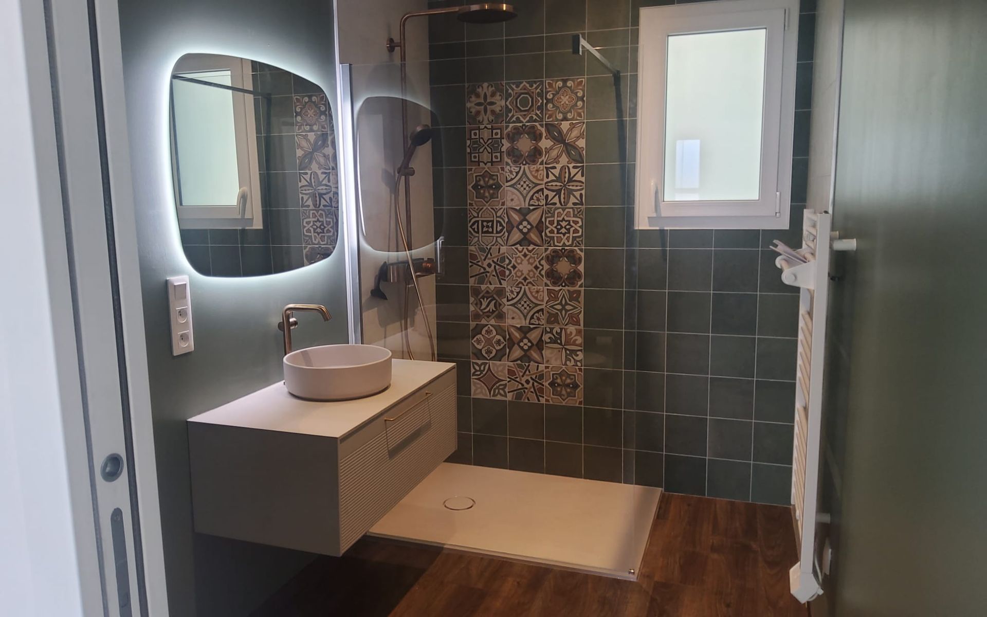 Salle de bains moderne avec meuble-lavabo, miroir, douche carrelée et fenêtre.