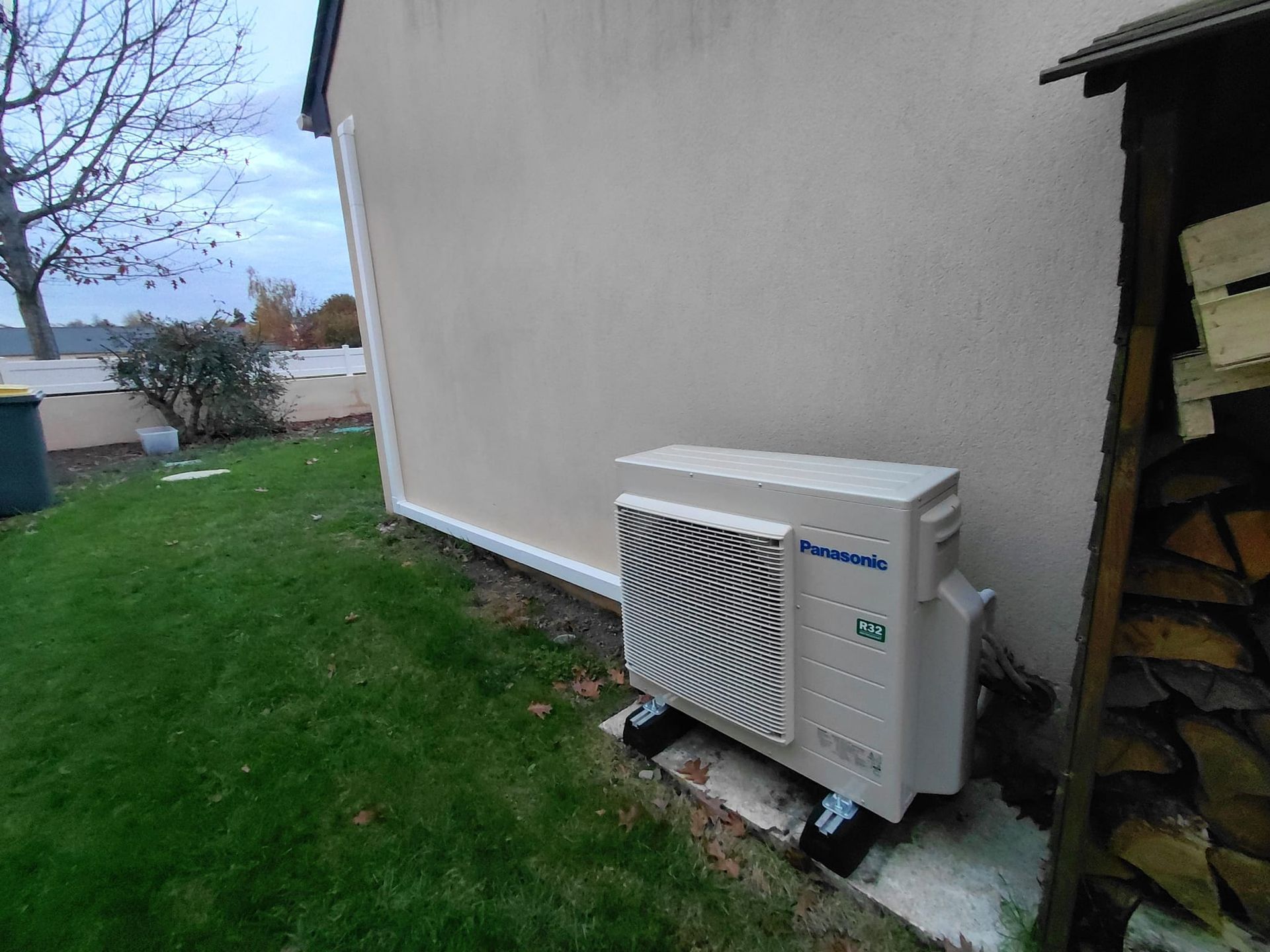 Unité de climatisation extérieure près d'un mur beige donnant sur une pelouse