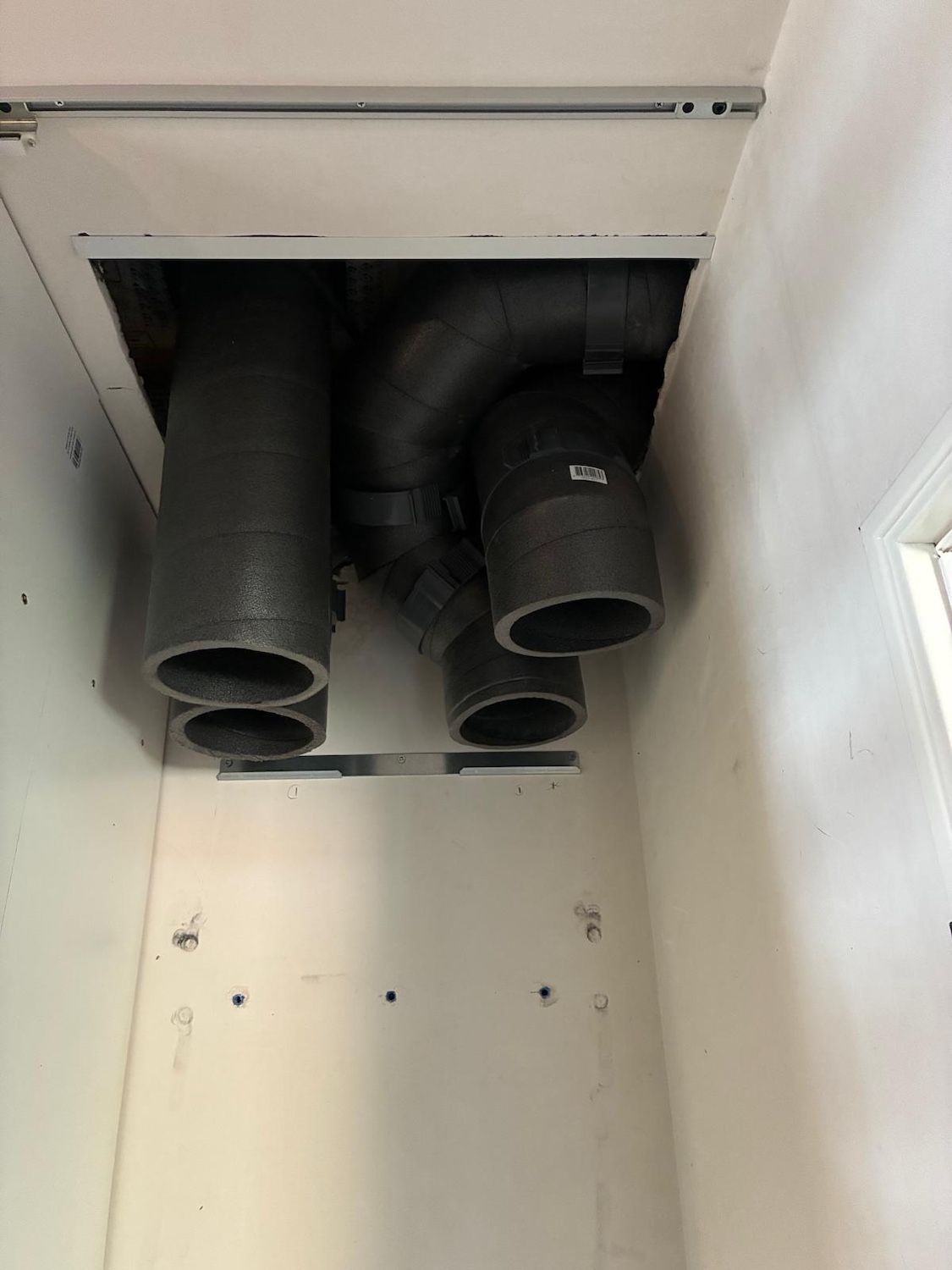 Ouverture de conduit de climatisation au plafond avec quatre tuyaux d'évacuation noirs dans une niche murale blanche