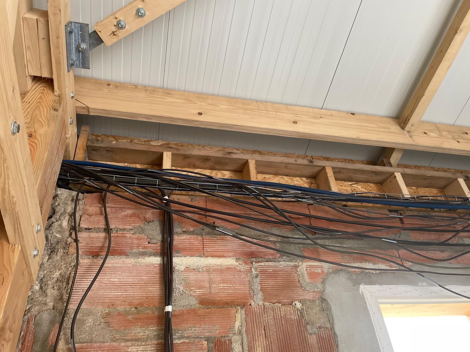 Câblage électrique apparent le long d'un mur de briques sous les poutres et chevrons en bois de la toiture.
