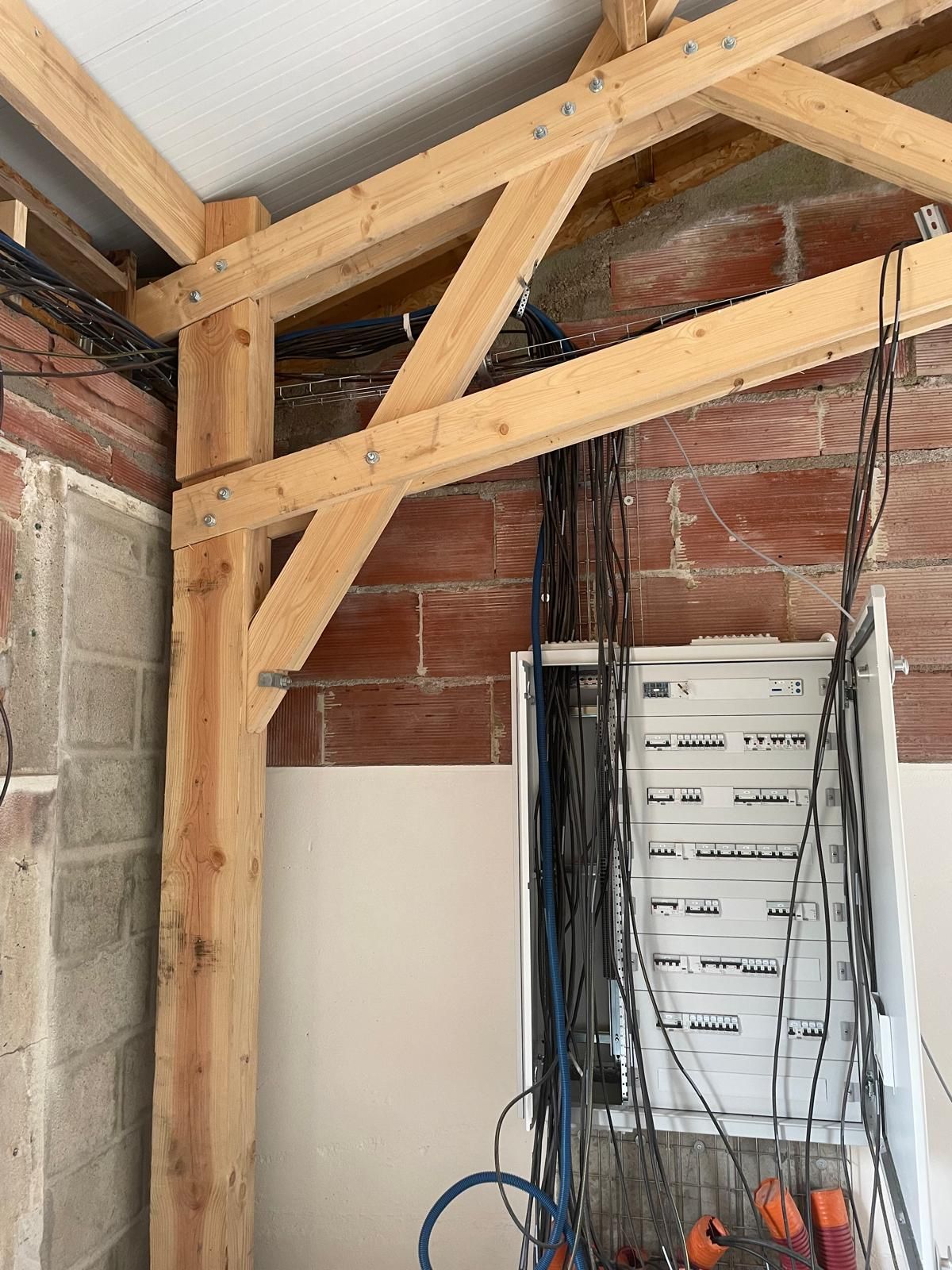 Charpente en bois apparente et mur de briques en cours de rénovation, avec des câbles qui pendent et une armoire sur la droite.