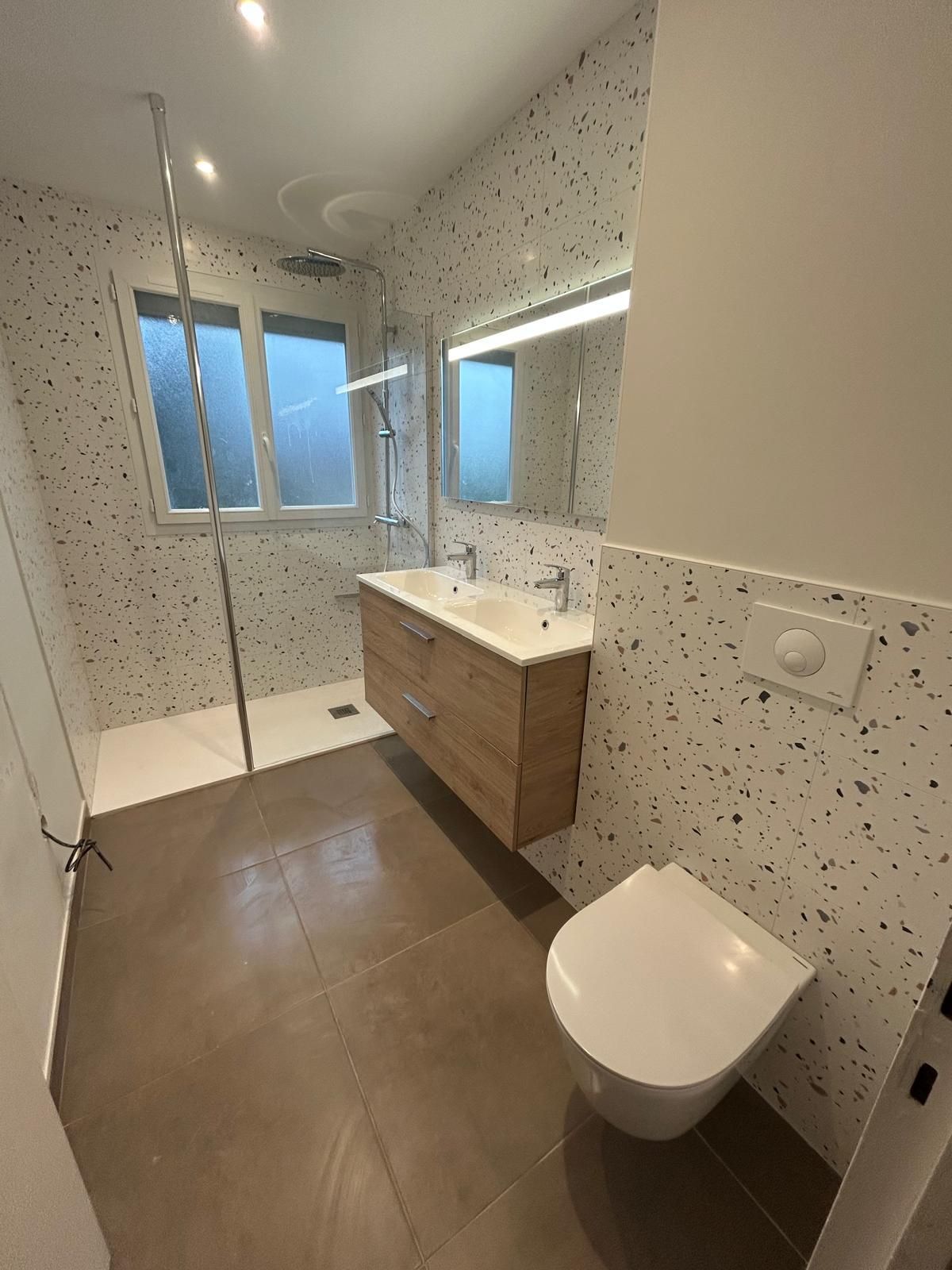 Salle de bains moderne avec douche à l'italienne, meuble-lavabo suspendu, toilettes suspendues et carrelage moucheté au sol et aux murs.