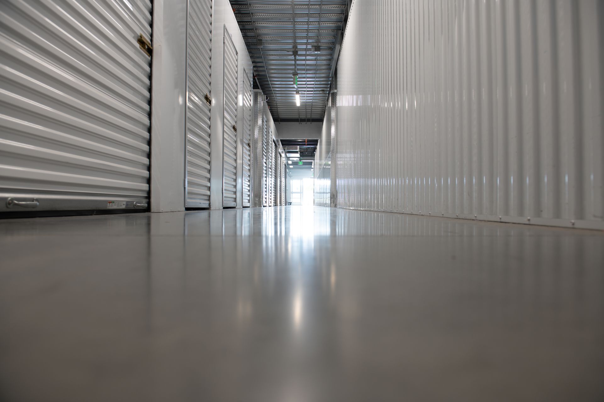 Long, clean hallway of an indoor drive-up storage facility with white metal unit doors