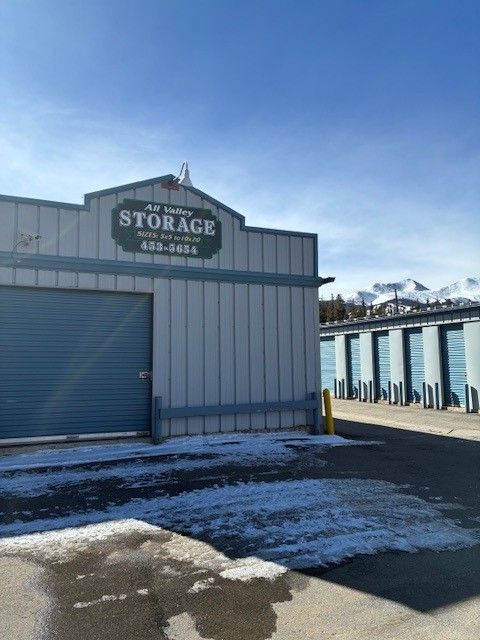 Storage facility with blue doors, sign, and snow on the ground; mountains visible in the distance.