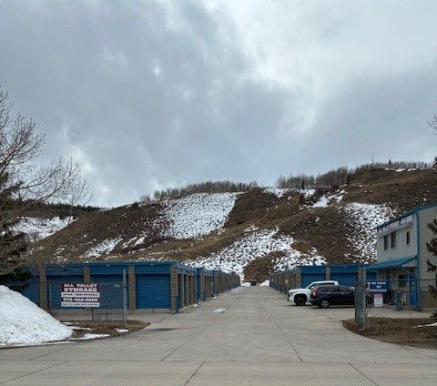 Red storage unit hallway. Metal doors line walls, bright overhead lights, concrete floor.