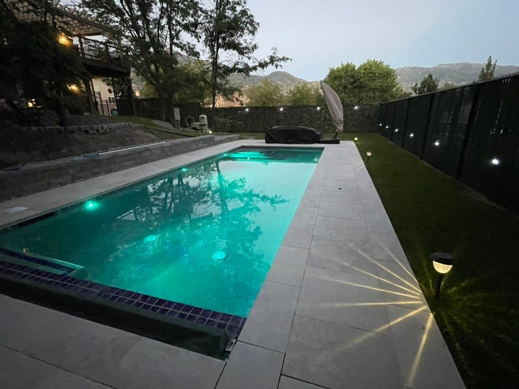 Pool with turquoise water, surrounded by a gray patio and green artificial grass. 