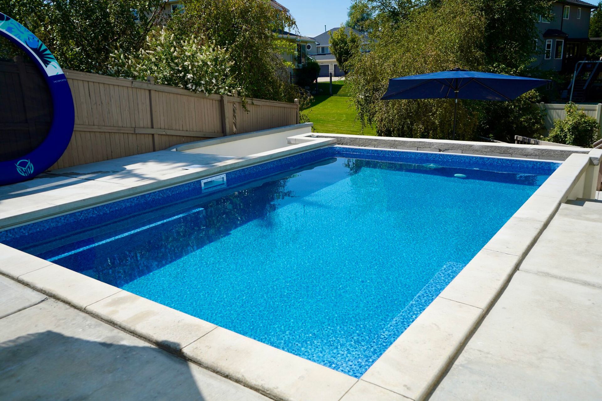 A rectangular in-ground swimming pool with blue water, surrounded by a concrete patio and a bamboo fence.