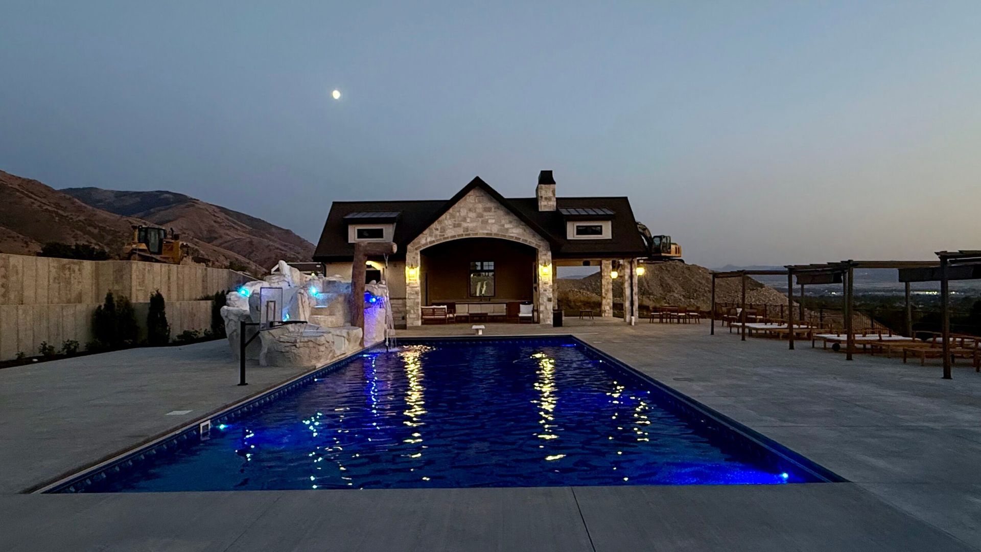 Pool at dusk, illuminated with blue lights, in front of a stone-clad building with a covered patio.