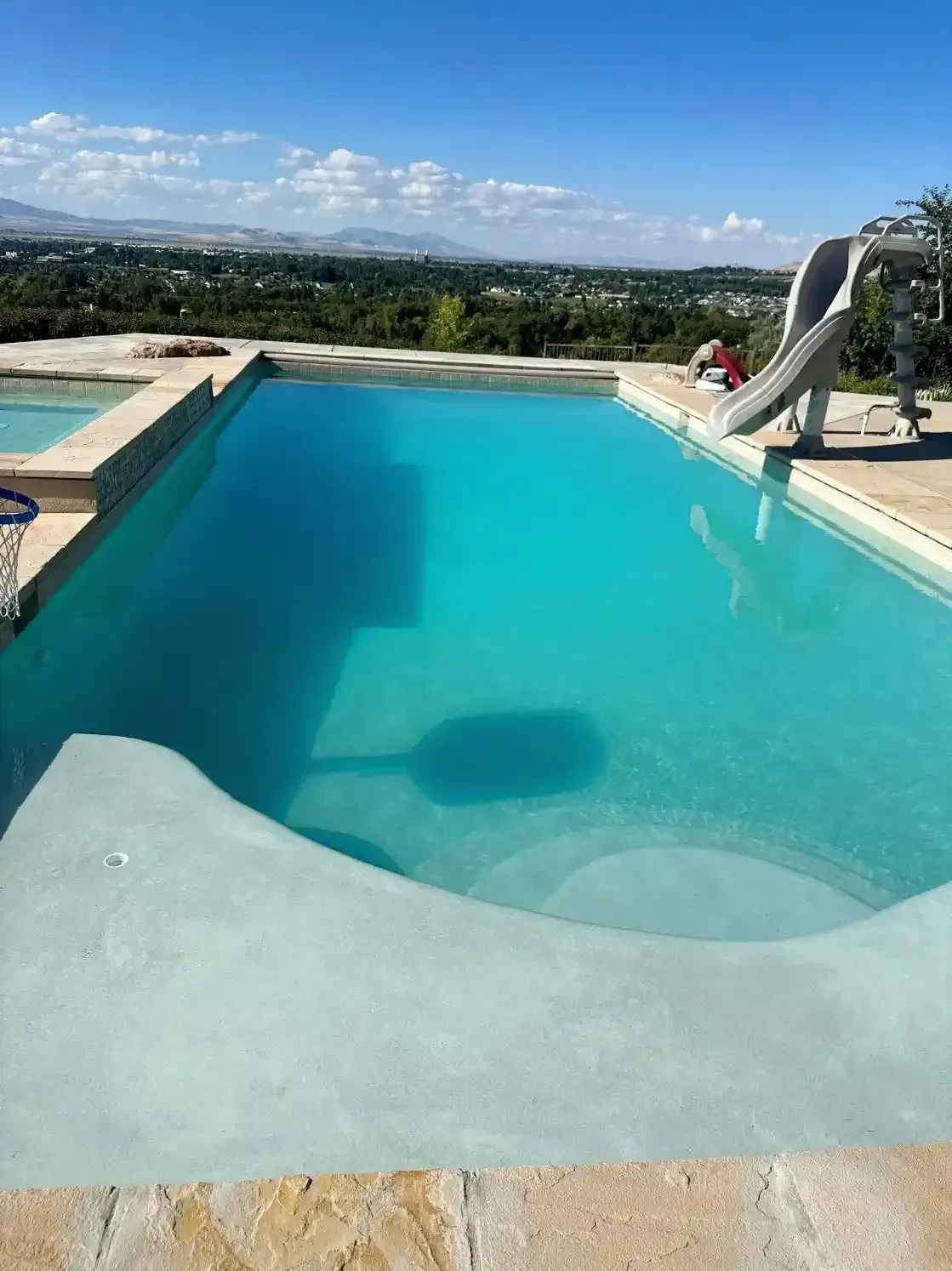 Swimming pool with slide, blue water, overlooking a green landscape and clear sky.