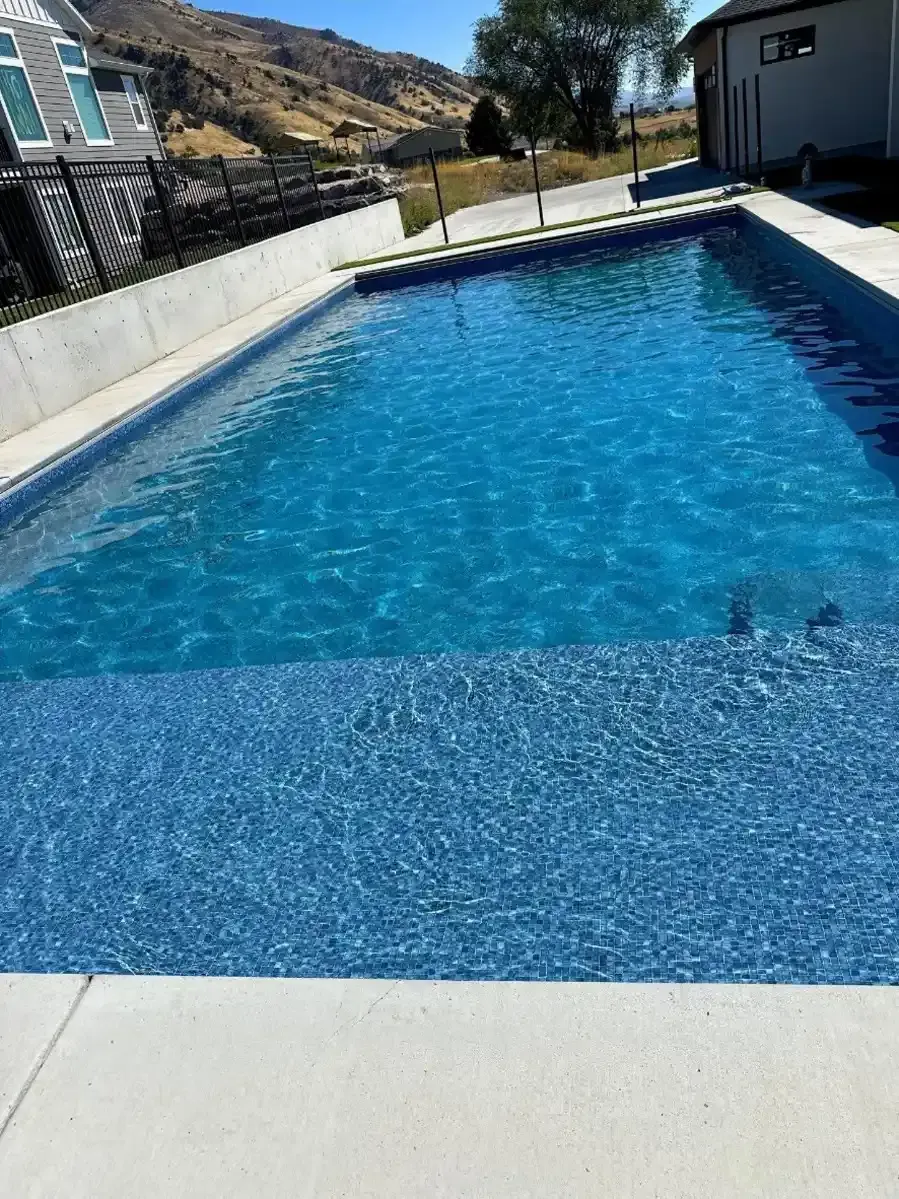 A rectangular outdoor swimming pool with blue water and light-colored concrete edges.