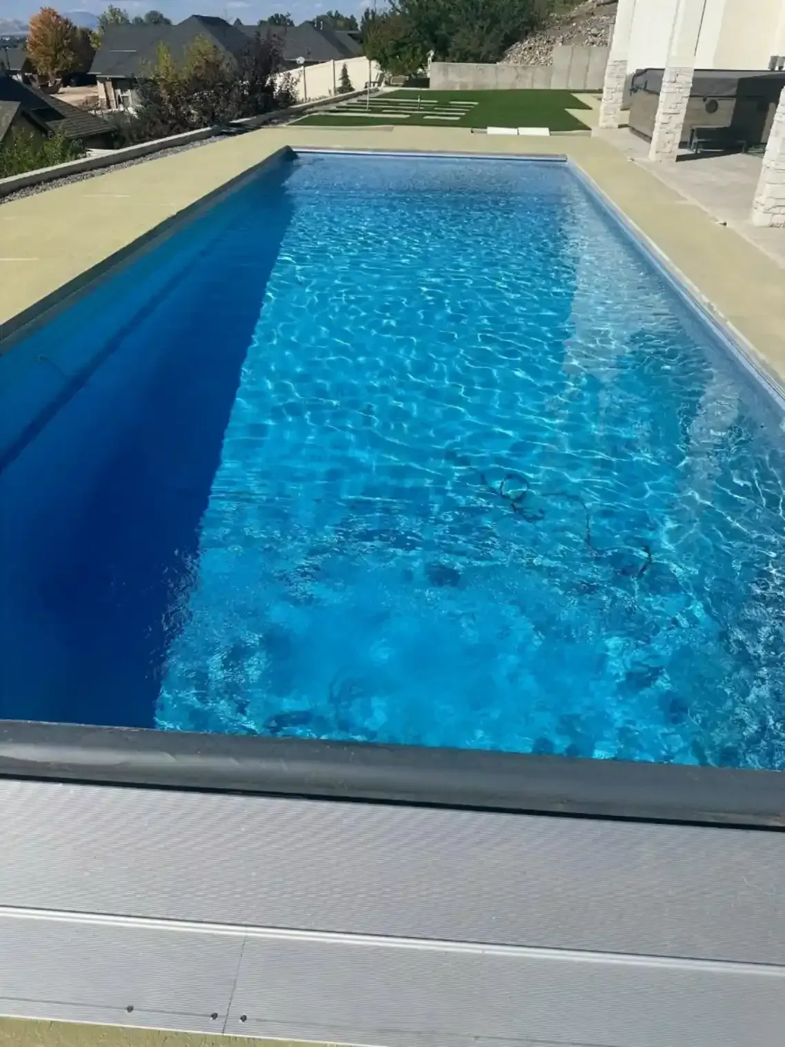 Rectangular blue pool with a partially covered gray retractable cover. Yellow concrete surrounds the pool.