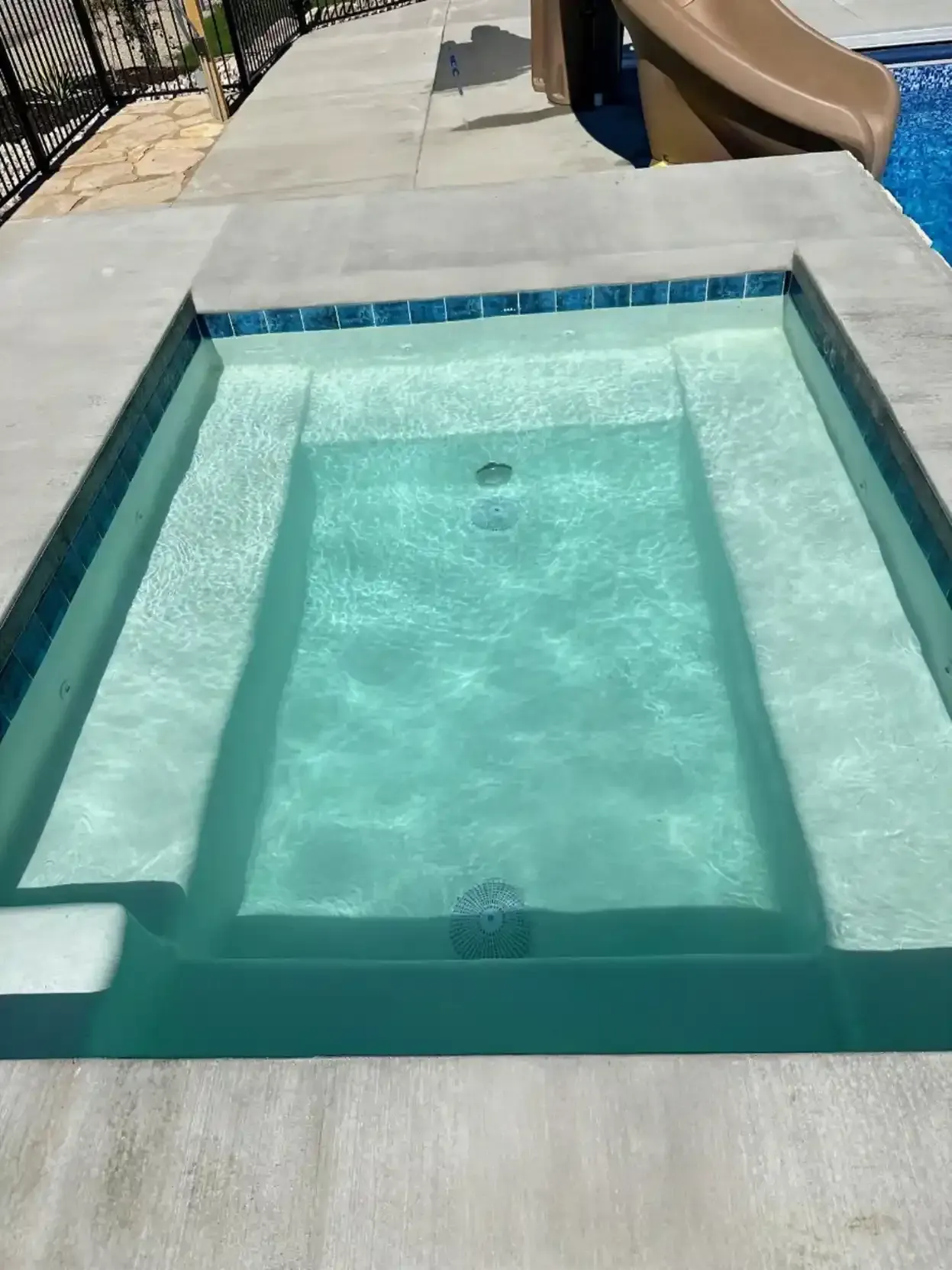 A small, in-ground spa with steps, filled with clear water, surrounded by concrete.