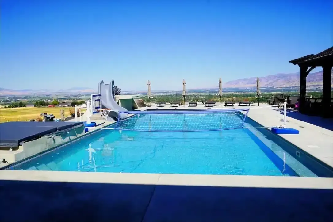 Large rectangular pool with a water slide, overlooking a valley under a clear blue sky.
