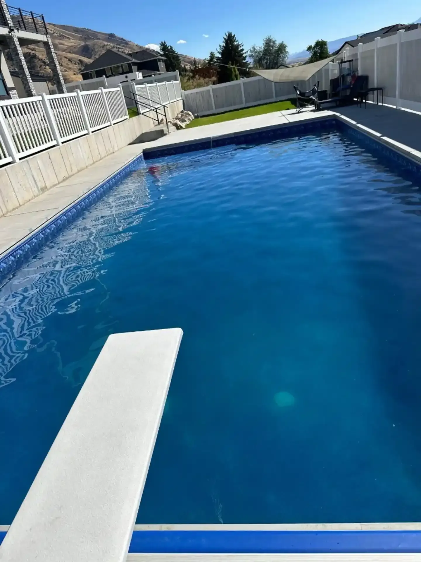 Pool with diving board. Blue water, white fence, sunny outdoors.