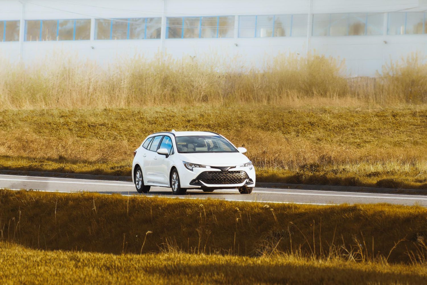 A white car is driving down a road next to a field.