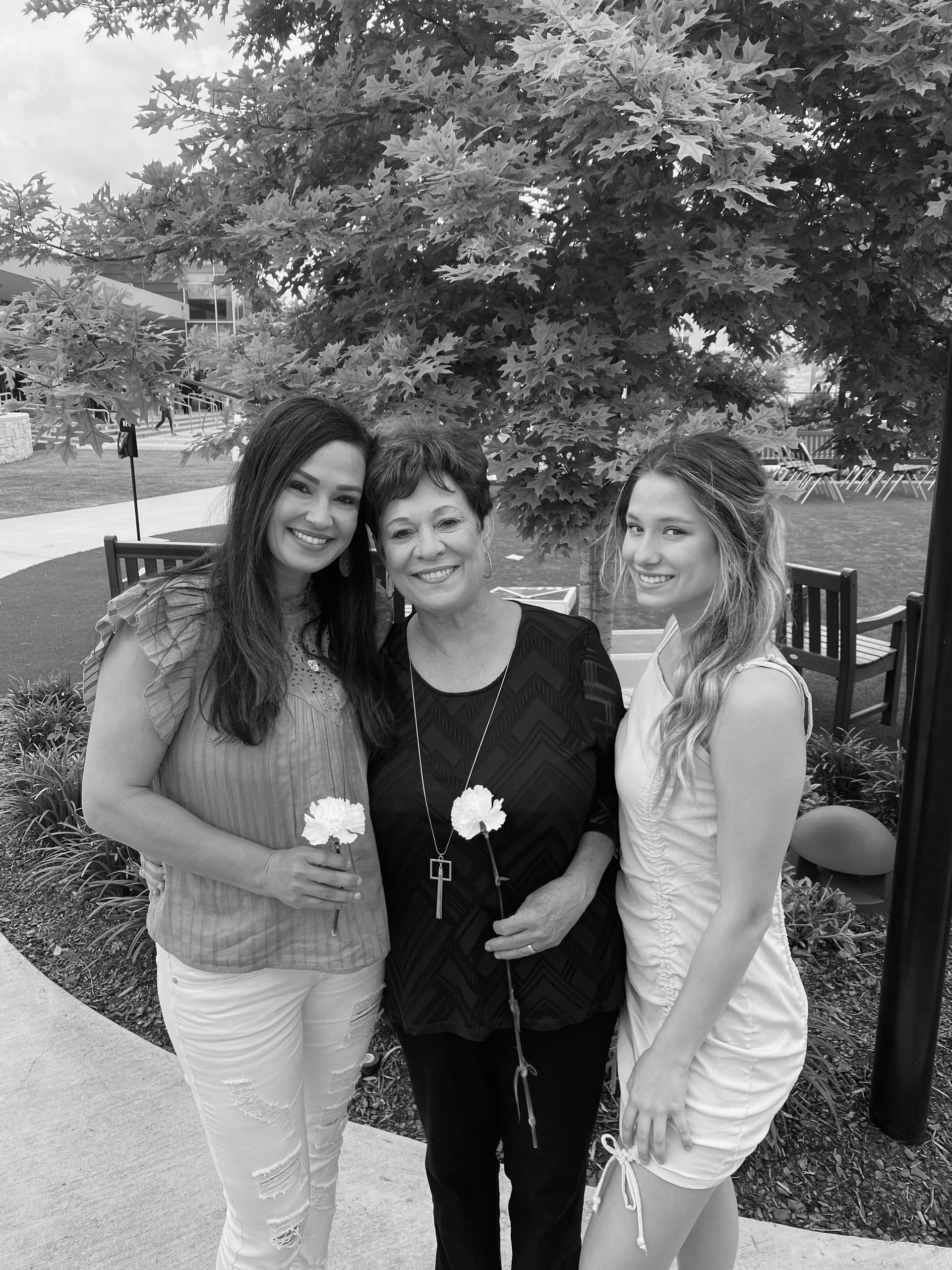 A black and white photo of Zoey, her mother, and her grandmother standing next to each other holding flowers.