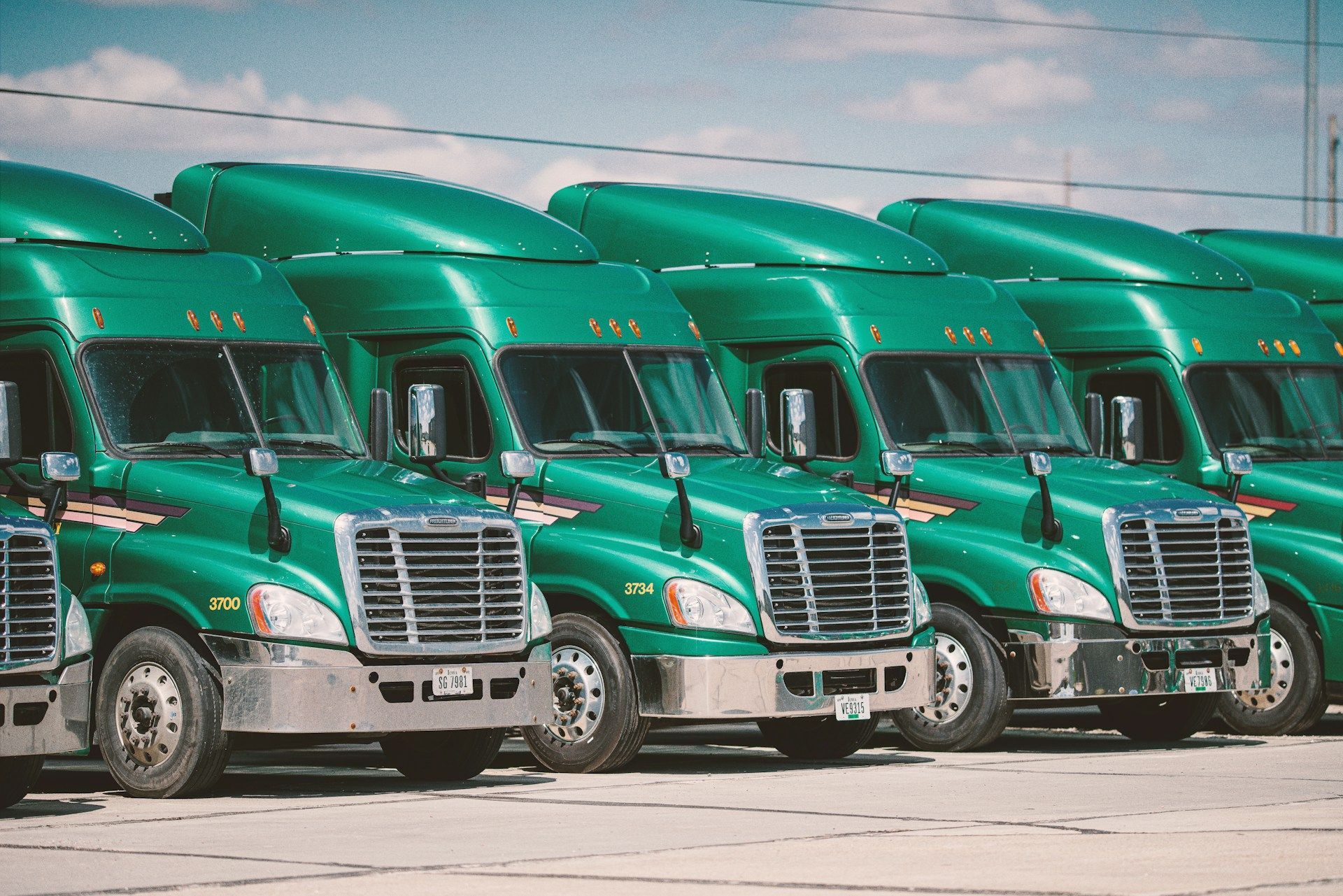 A row of green semi trucks are parked in a parking lot.